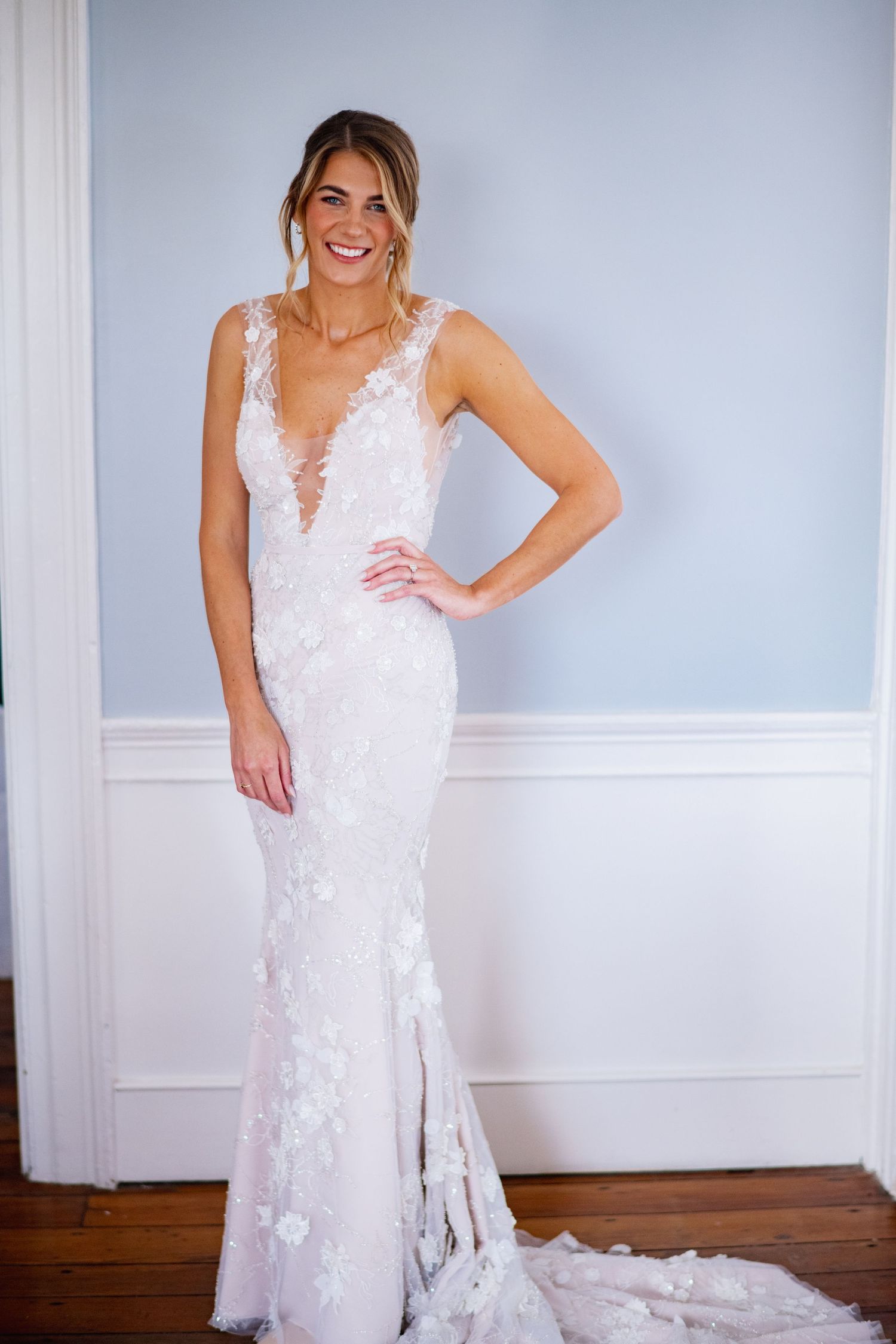 A stunning white lace wedding dress with delicate floral appliques is showcased against a light gray backdrop.