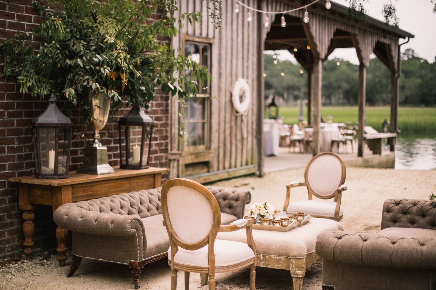 Vintage-style seating arrangements with elegant beige upholstered chairs and sofas in a rustic wedding venue setting.