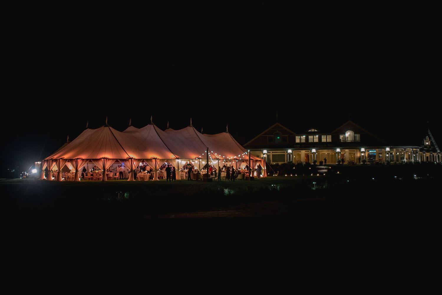Illuminated wedding tent glows warmly against dark night sky during outdoor evening reception celebration.