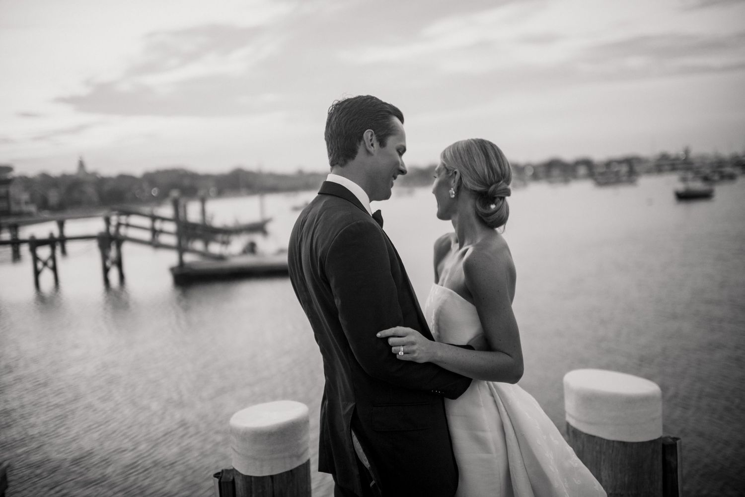 Black and white portraits of a couple embracing near a dock at sunset.