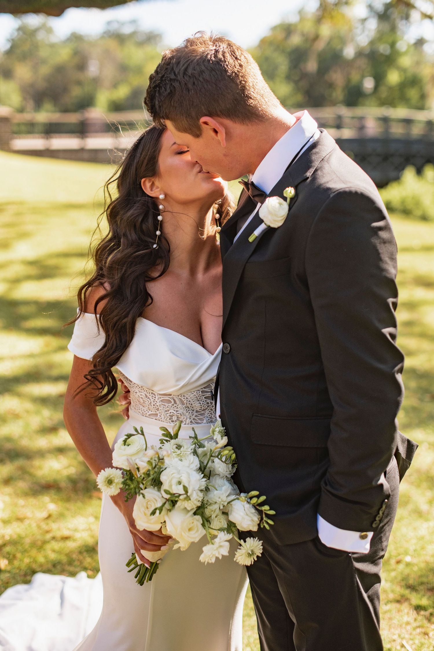 Romantic wedding couple sharing an intimate moment in golden sunlight with white bouquet.