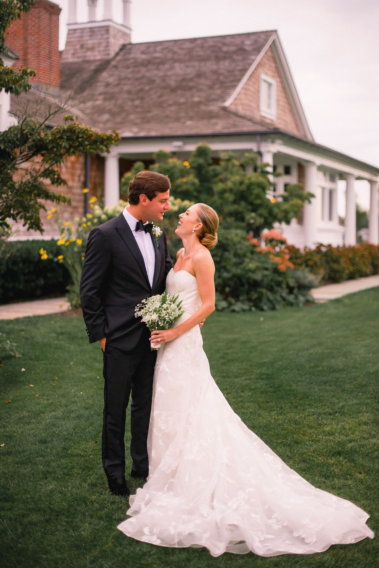 Wedding couple embracing on a lawn in front of a historic house with white columns.