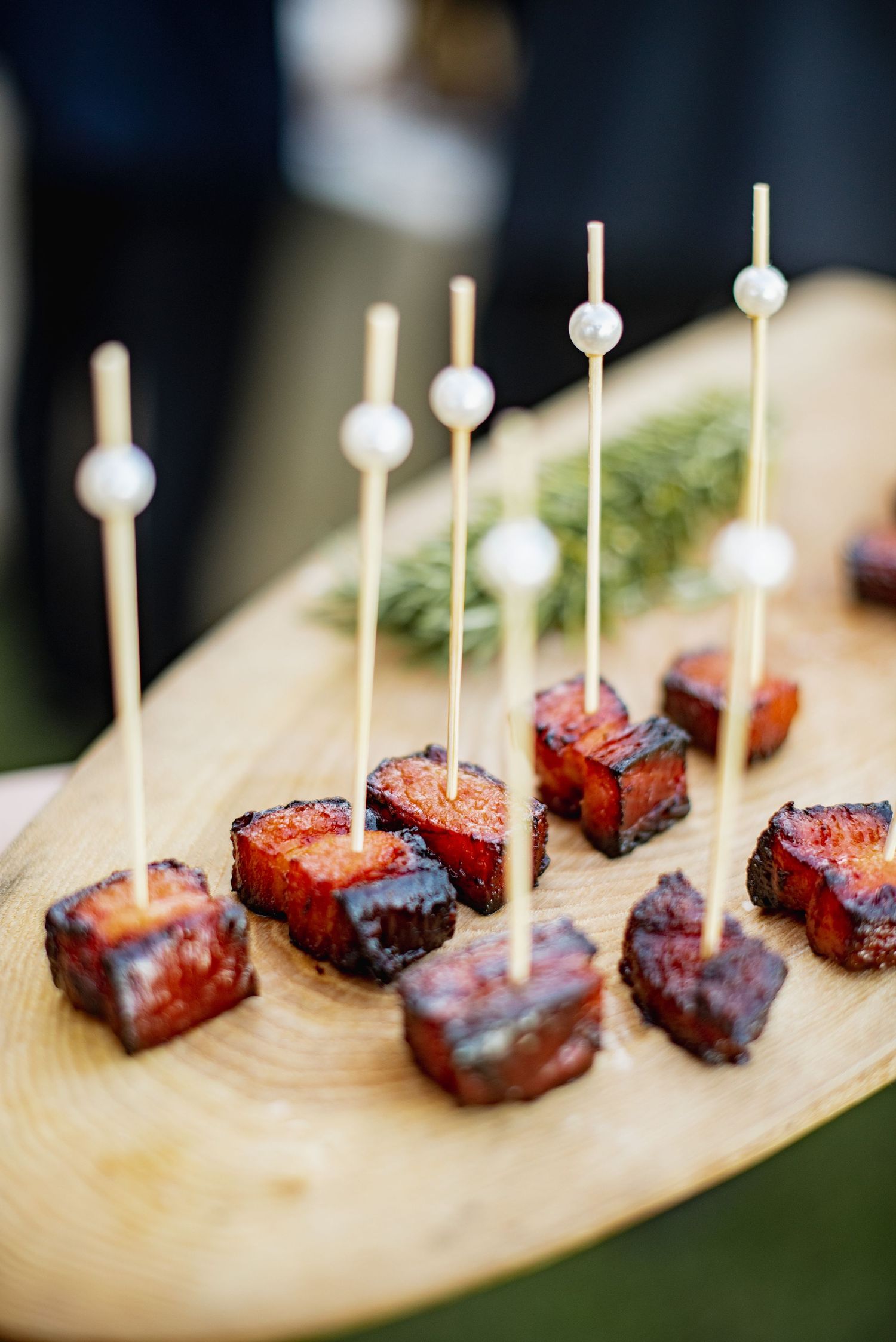 Grilled meat appetizers served on wooden plank with white toothpicks at an upscale catering event.