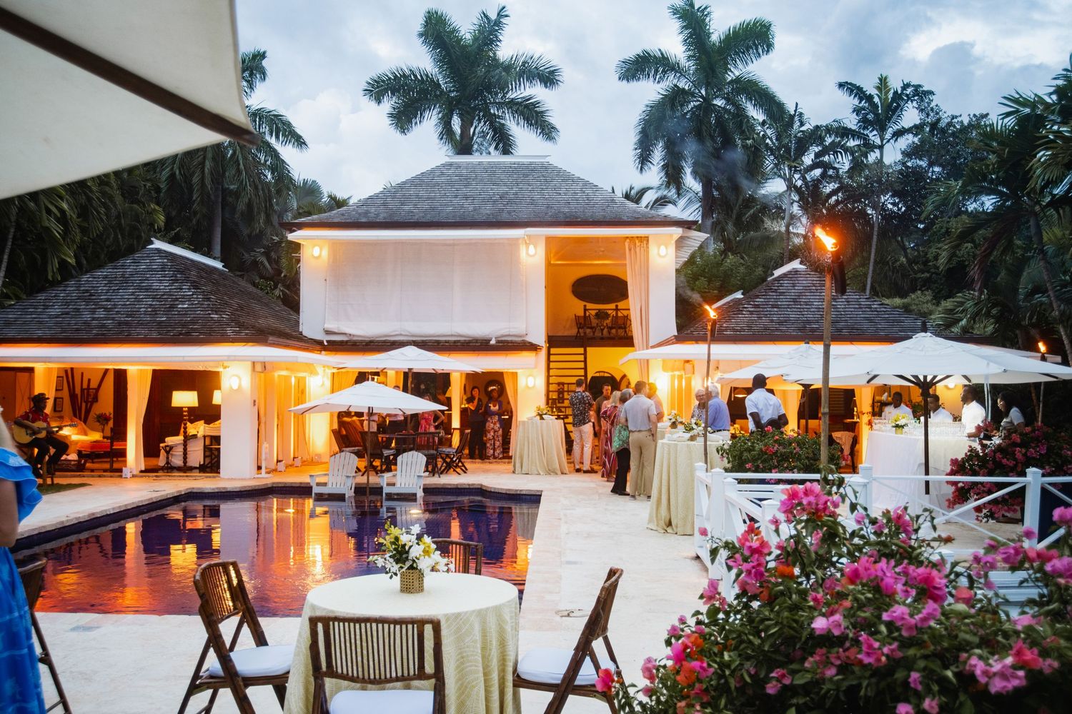 Luxurious tropical resort patio with glowing lights, palm trees, and outdoor seating areas at dusk.