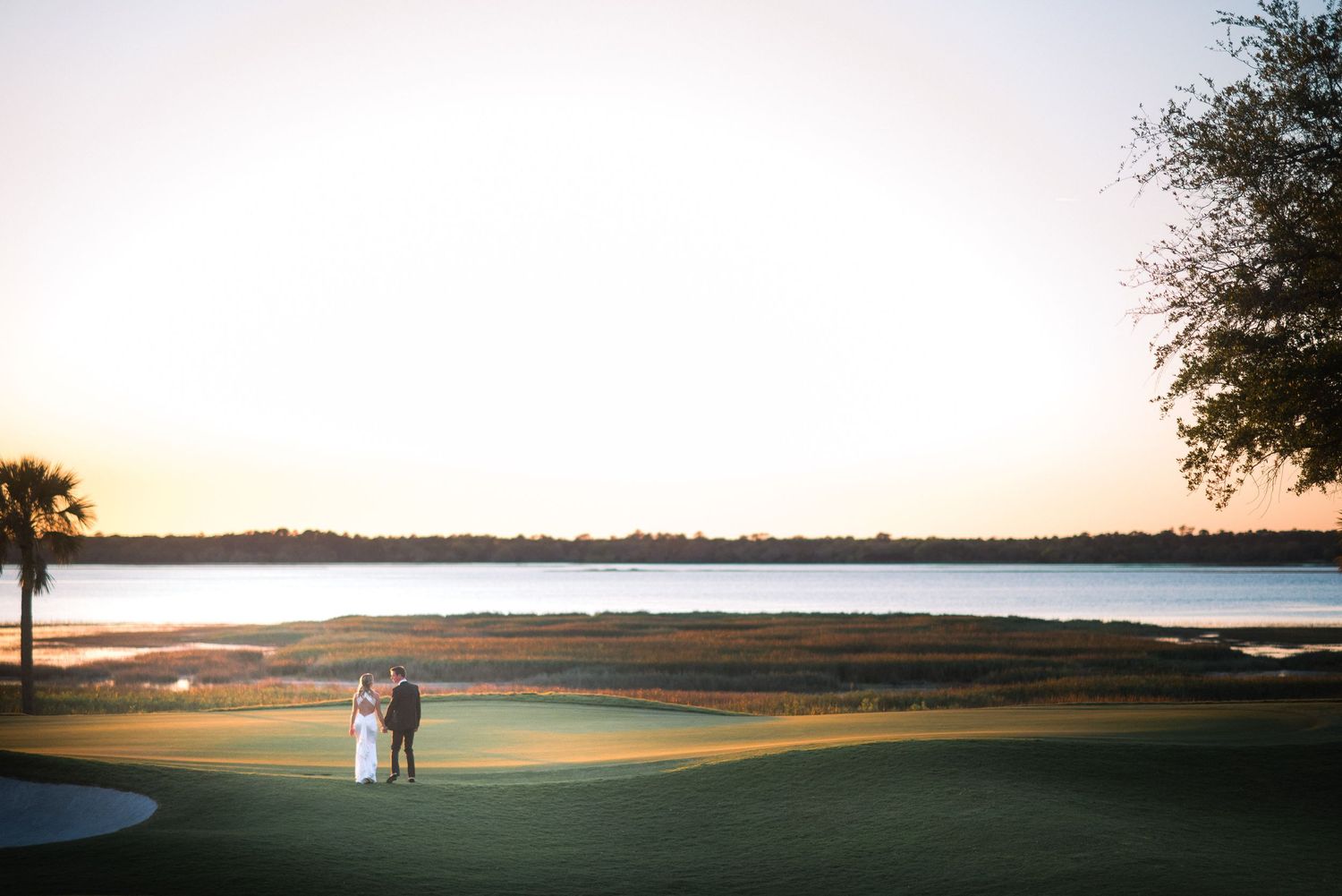 A couple strolls along a scenic golf course overlooking a tranquil lake at sunset.