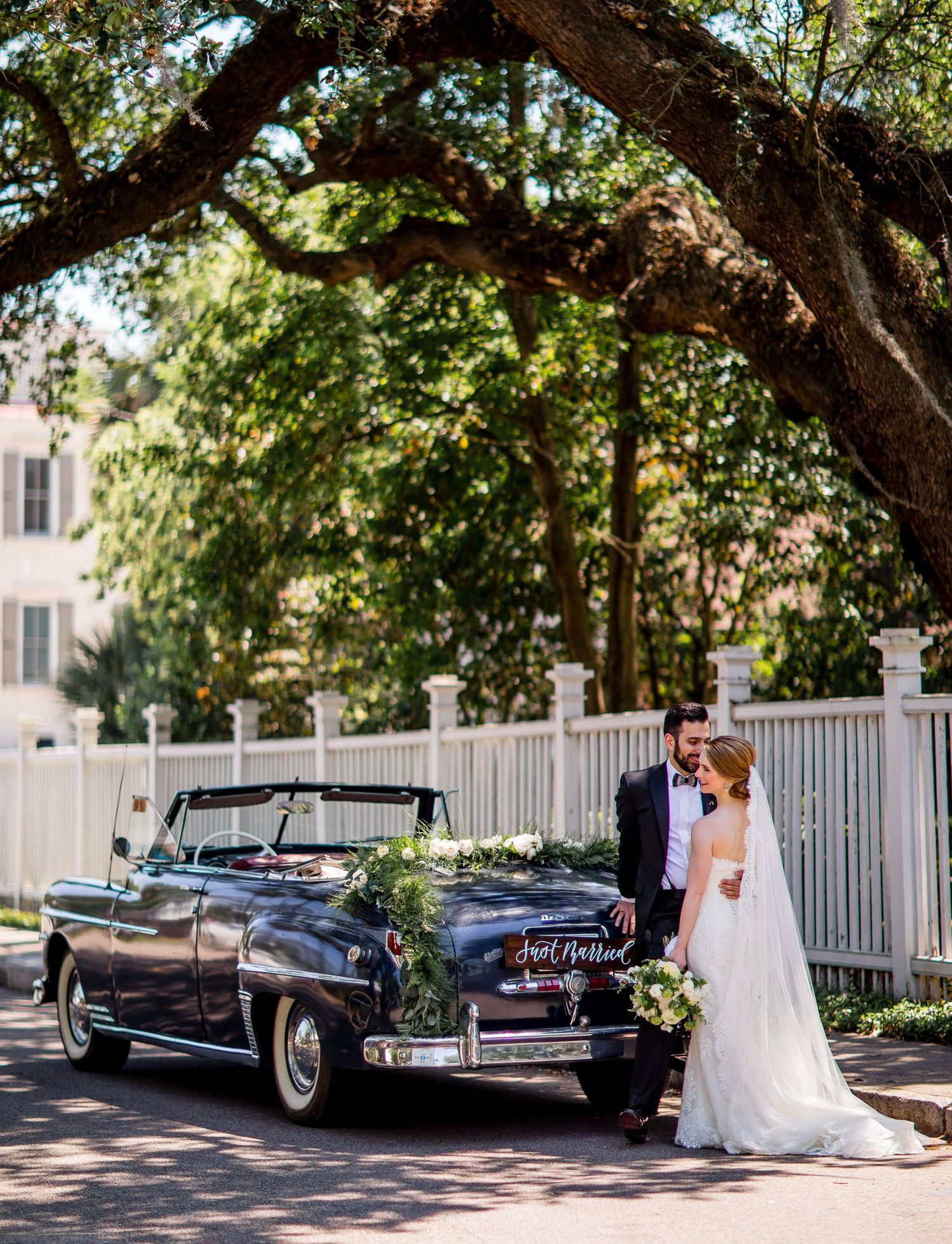 Classic vintage cars parked along a tree-lined street with a couple celebrating their wedding day.