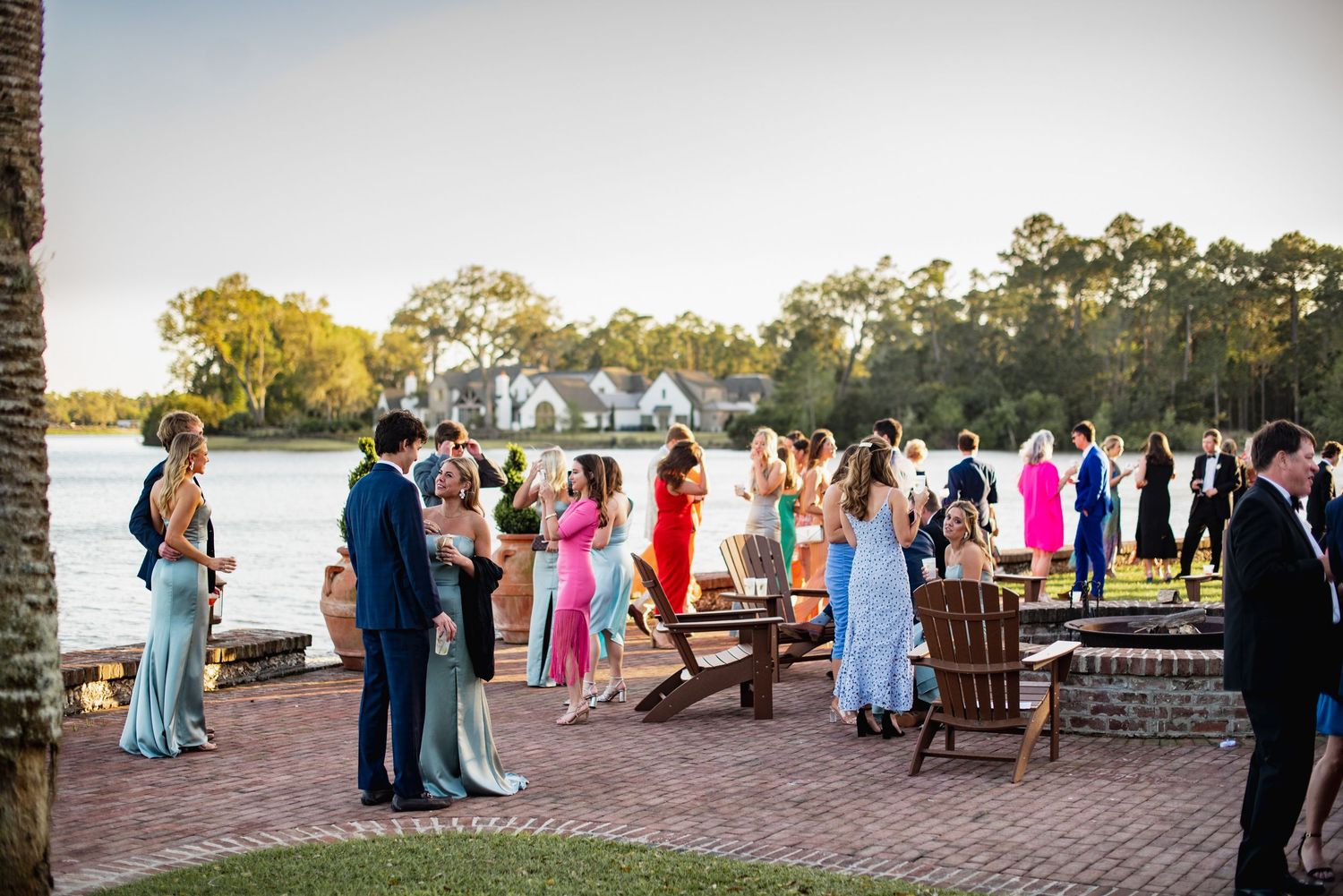 Wedding guests gather along a waterfront patio during sunset at an outdoor reception celebration.
