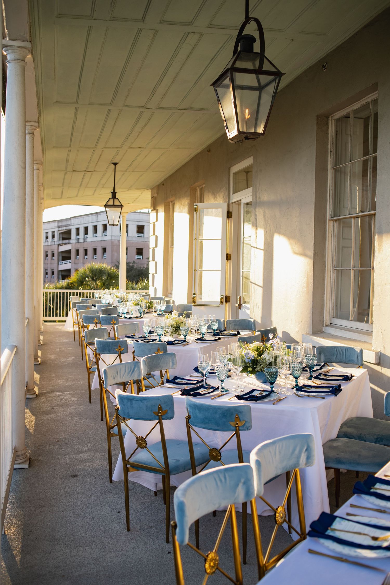Elegant outdoor dining patio with white tablecloths and blue upholstered chairs under a covered veranda.