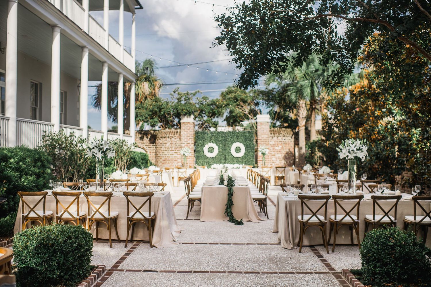 Outdoor wedding ceremony setup with white chairs and floral arrangements along a garden path.