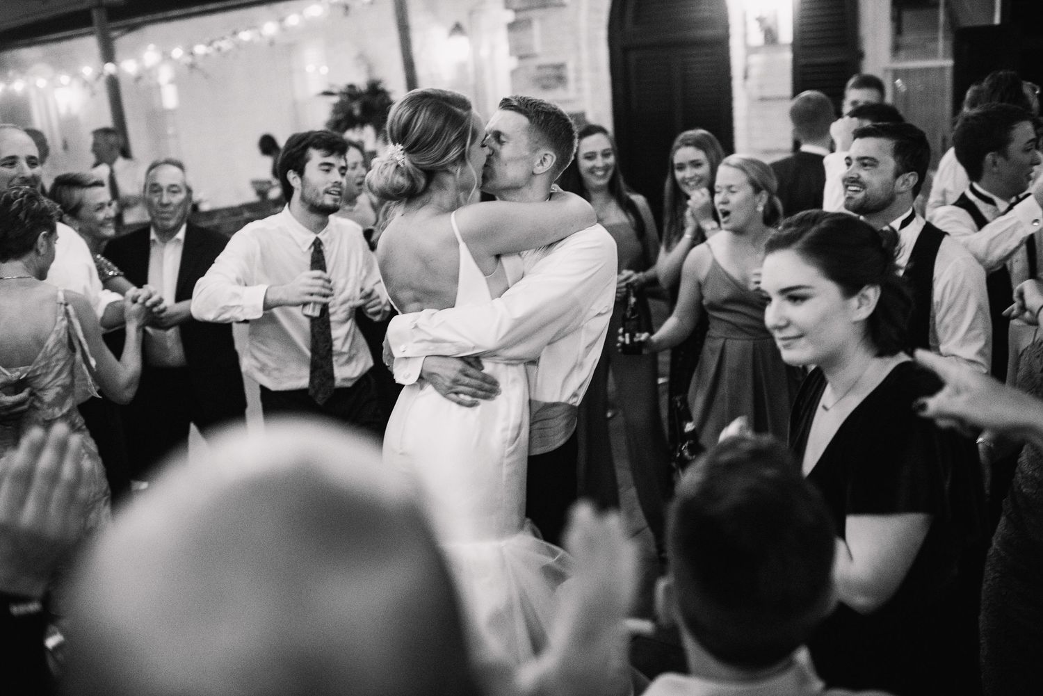 People dance and celebrate together at a lively indoor wedding reception with string lights overhead.