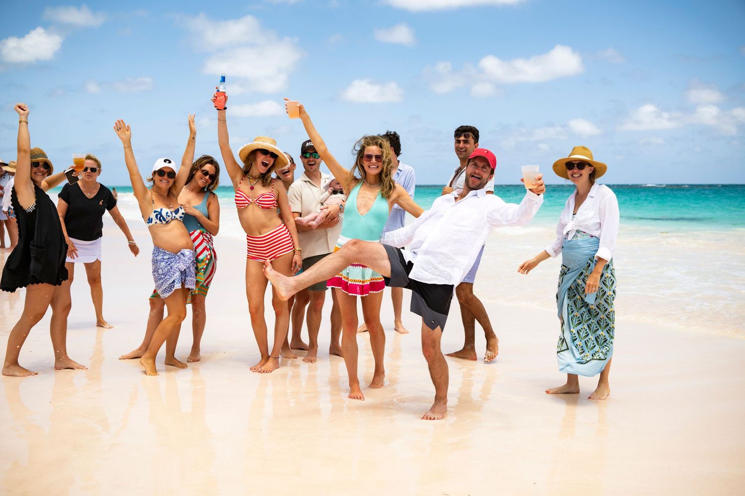 A group poses together on a pristine beach with turquoise waters and white sand in the background.