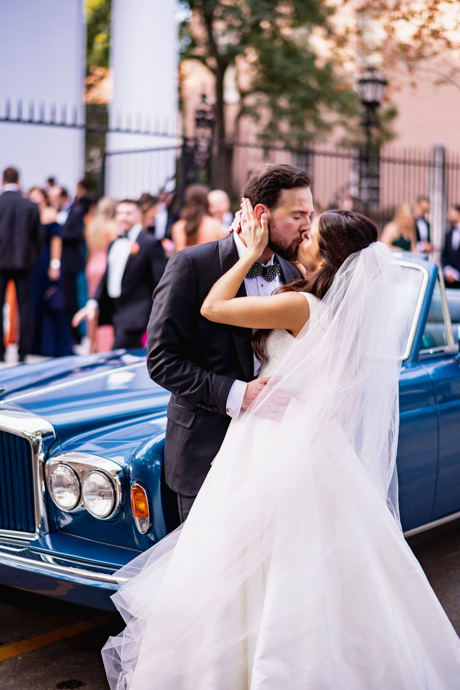 Romantic wedding couple poses with vintage blue car during sunset celebration.
