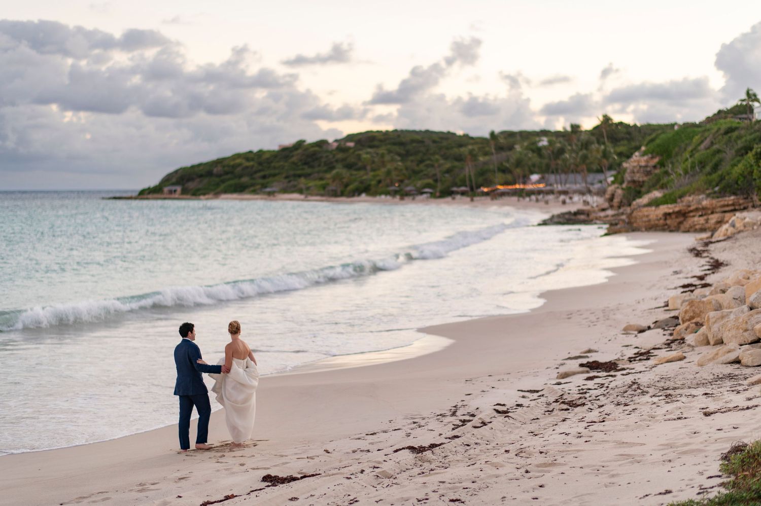 Couple walking along a scenic beach shoreline at sunset.
