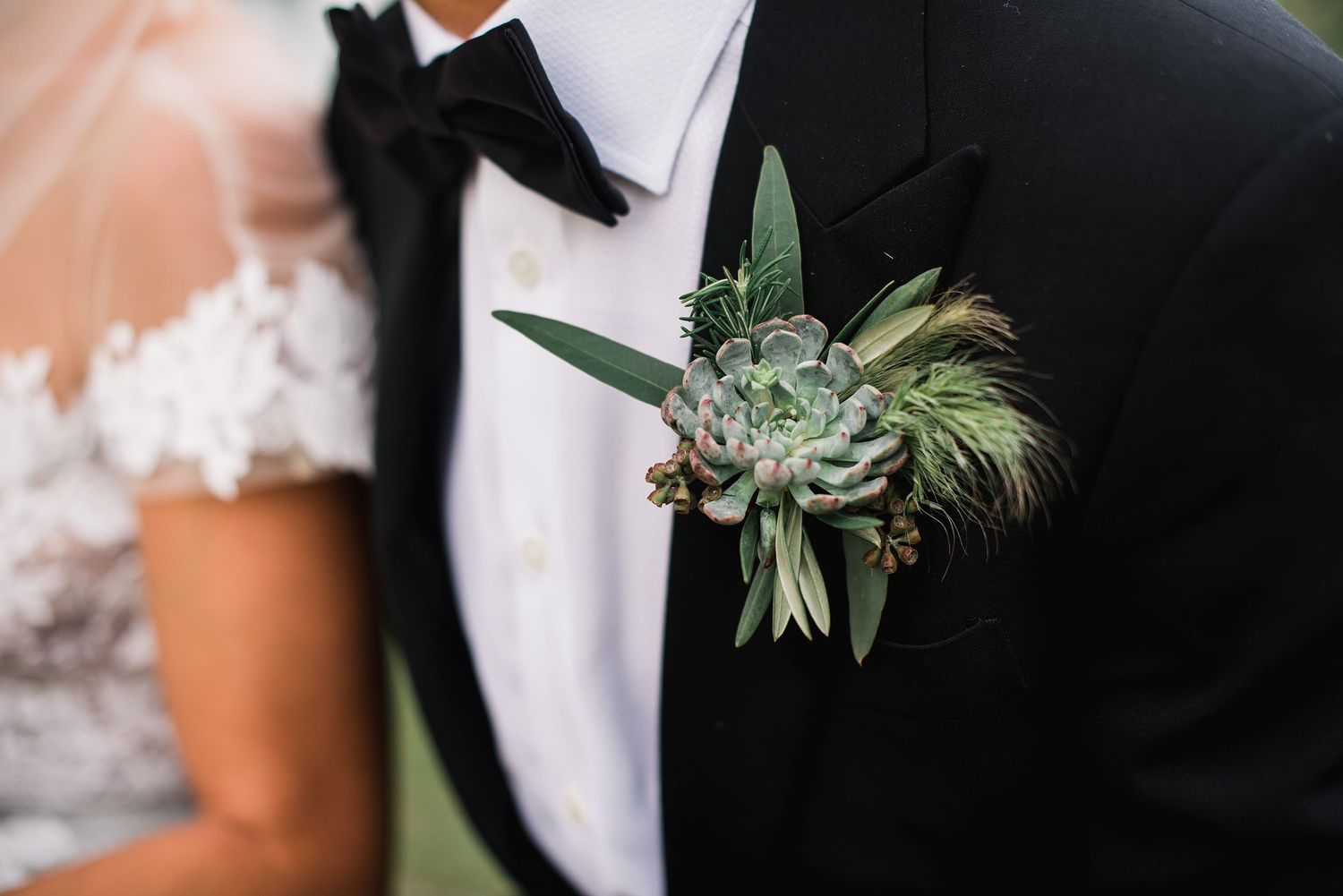 Wedding couple holds hands in elegant black and white attire with greenery accents in the background.