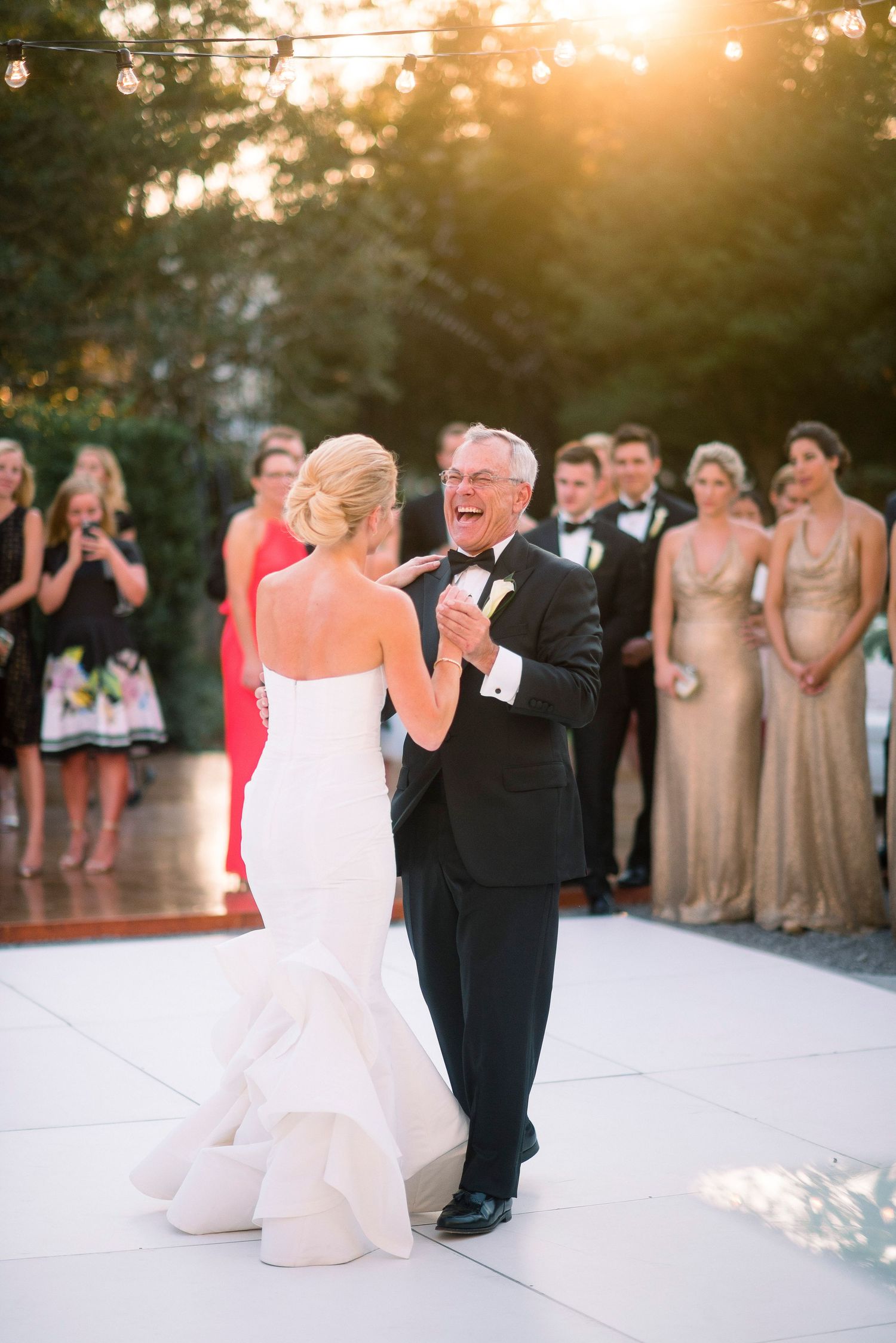 A bride and father share a joyful dance moment at an outdoor wedding reception during golden hour.
