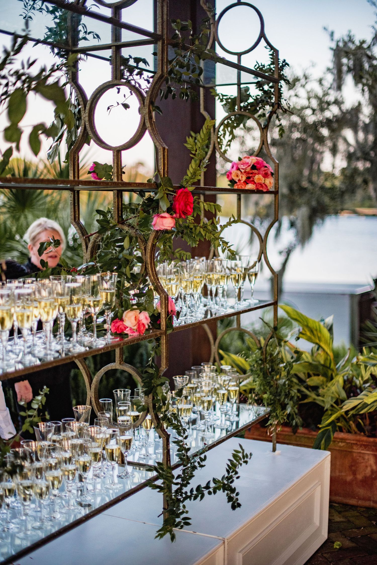 Elegant wedding reception table setting with crystal glasses and floral arrangements along an ornate iron railing.
