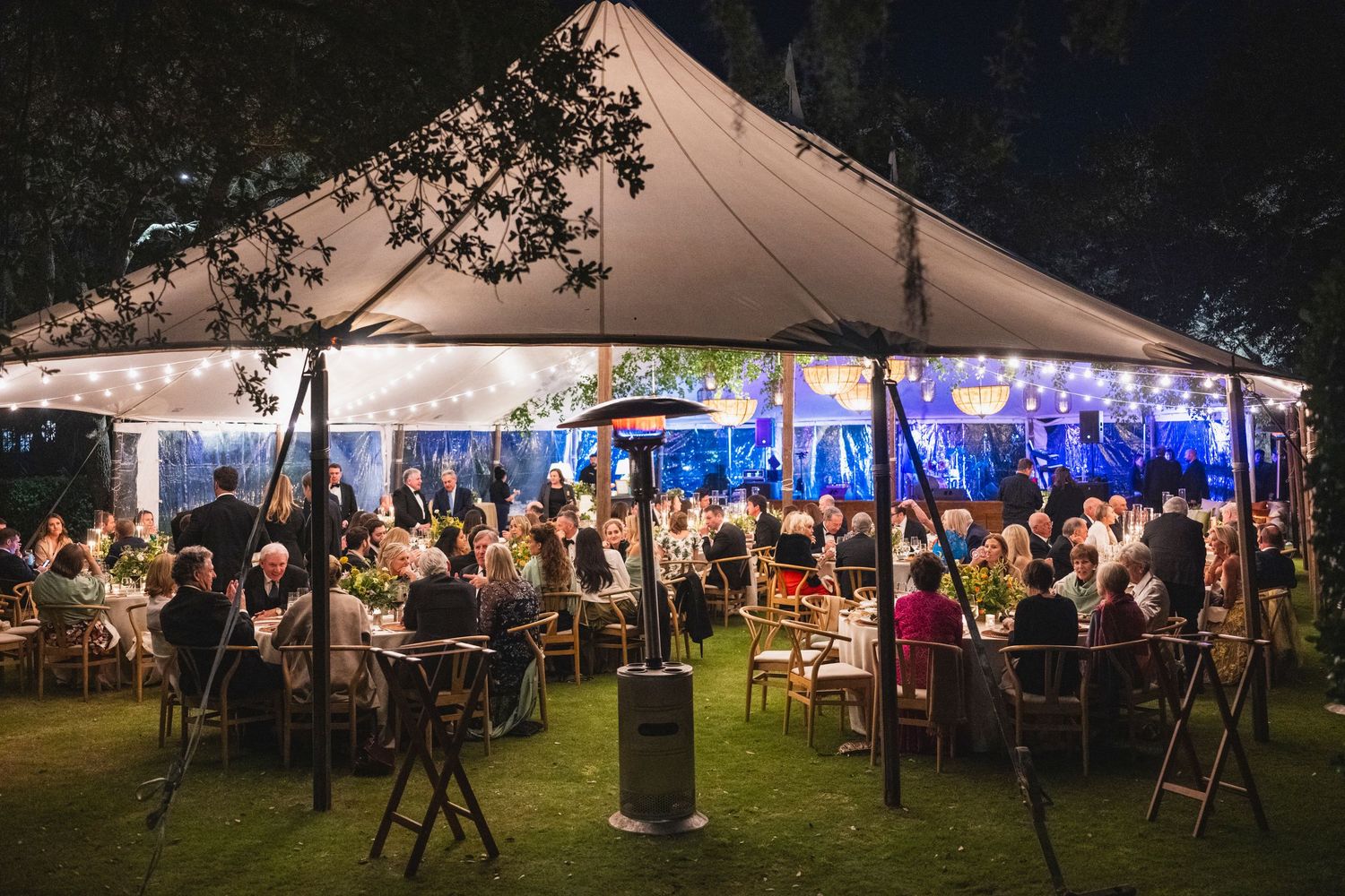 A series of outdoor event tents illuminated at night with guests mingling and celebrating under warm lighting.