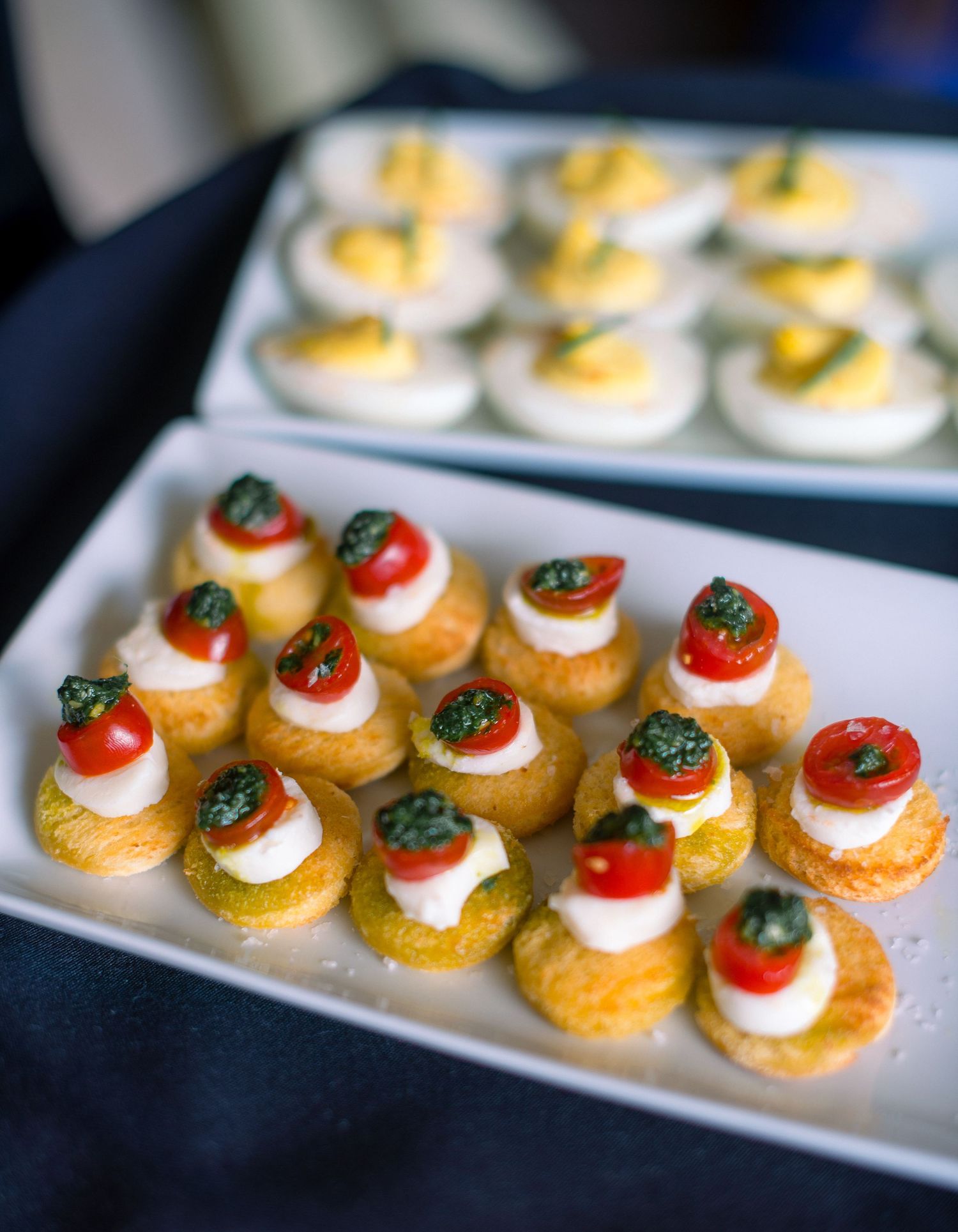 Elegant canapés with cherry tomatoes and whipped cream garnished with fresh herbs served on white platters.