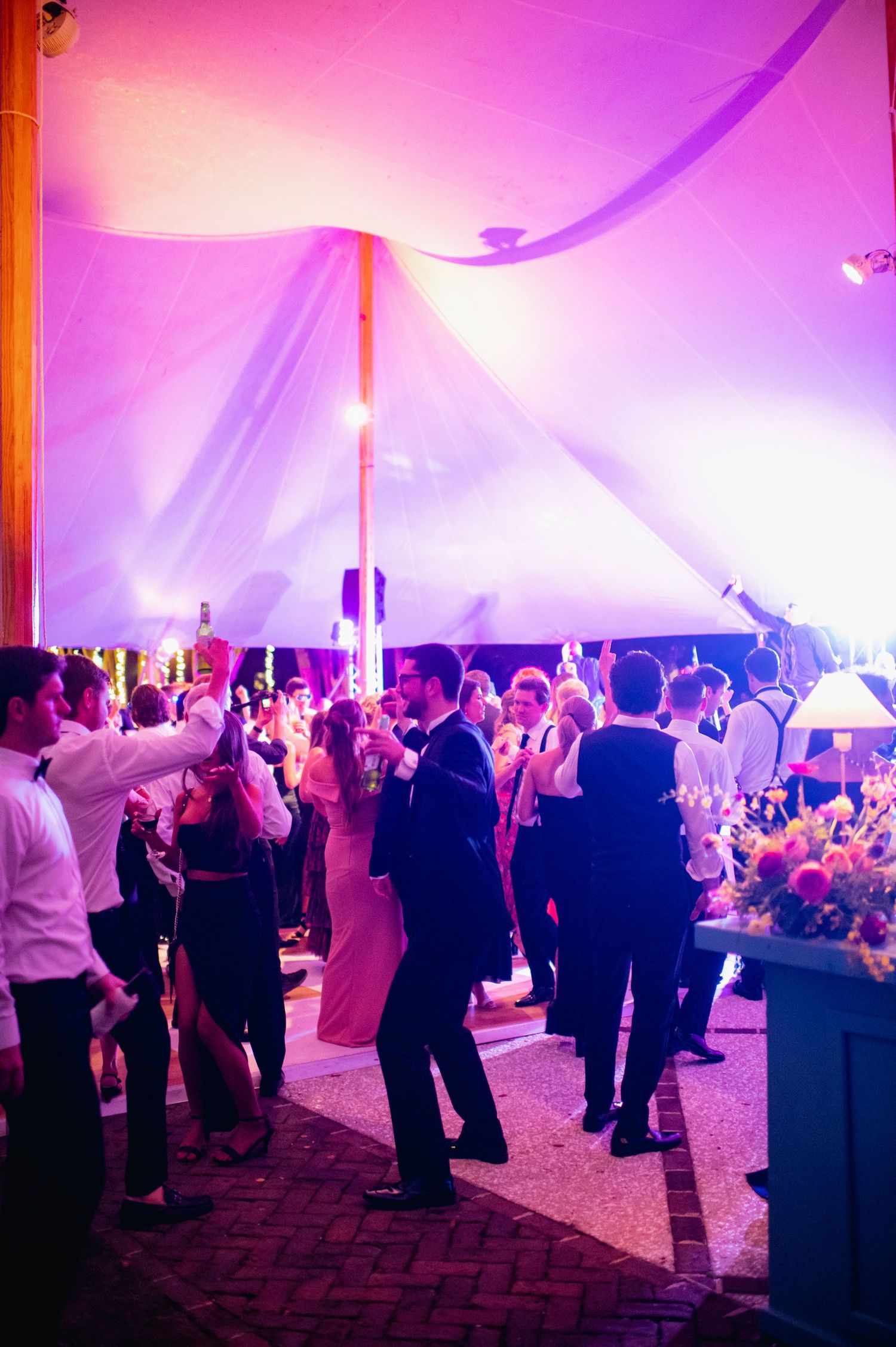 Wedding reception guests dancing on the dance floor under a tent with dramatic pink and purple lighting.
