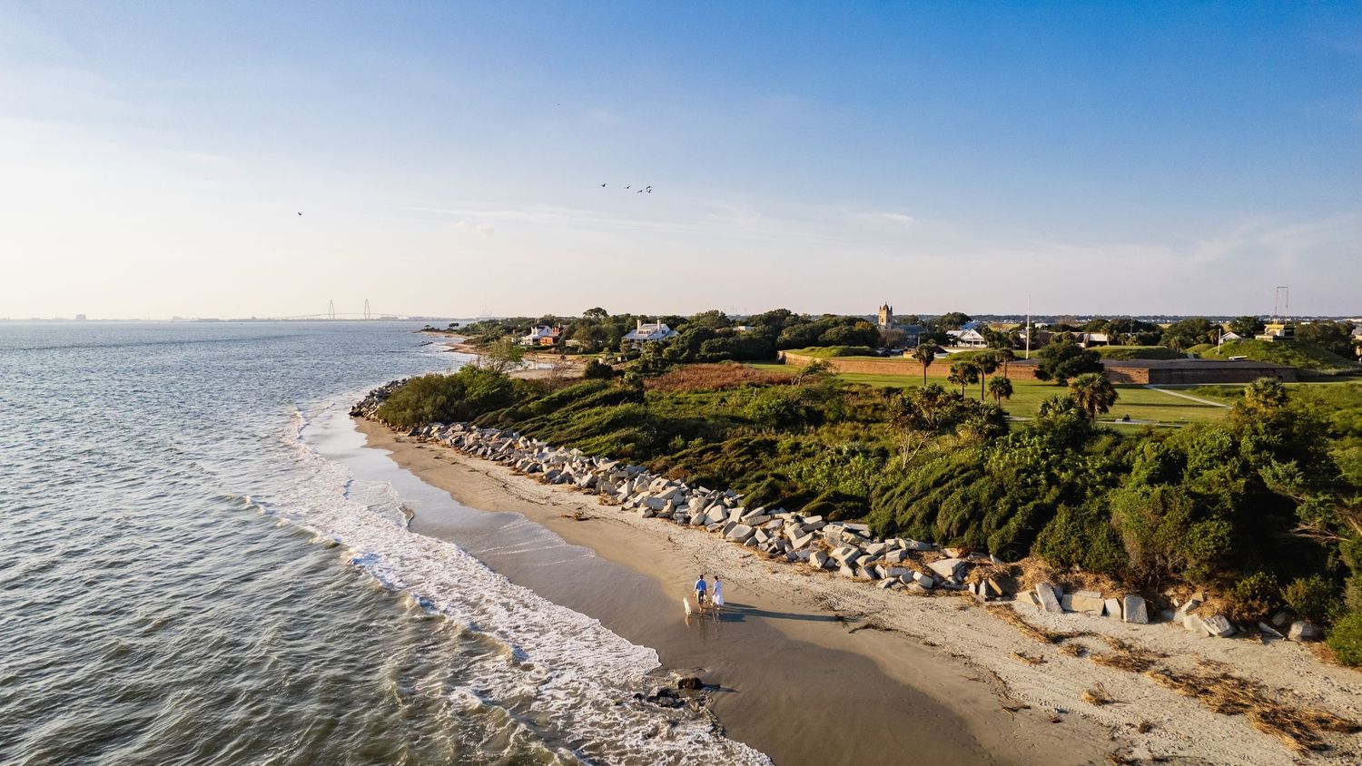 Panoramic aerial view of a sandy beach coastline with buildings and cliffs stretching along the ocean shore.