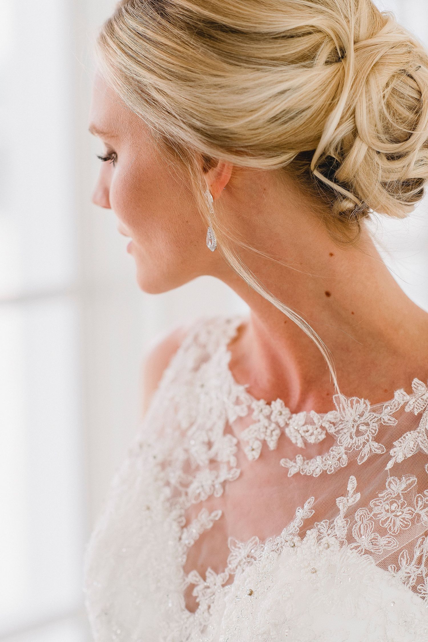 Close up profile view showing delicate lace details and elegant updo hairstyle with dangling earring.
