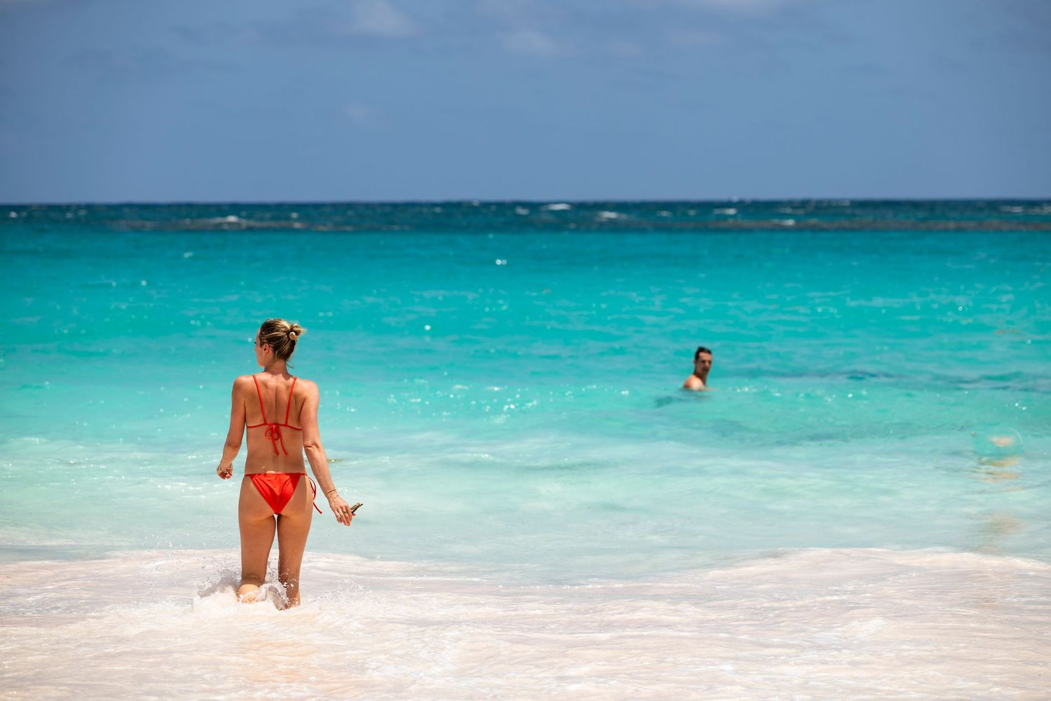 People enjoying a tropical beach with crystal clear turquoise waters and white sand on a sunny day.