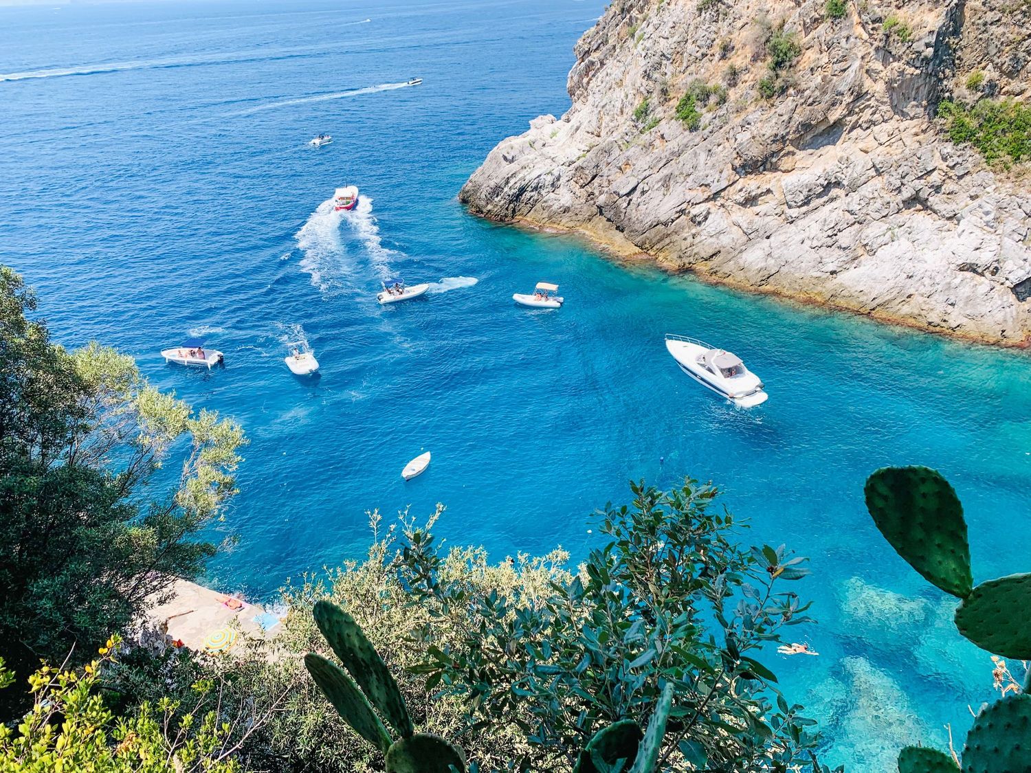 Aerial view of boats floating in a secluded turquoise cove surrounded by steep rocky cliffs in Praiaino
