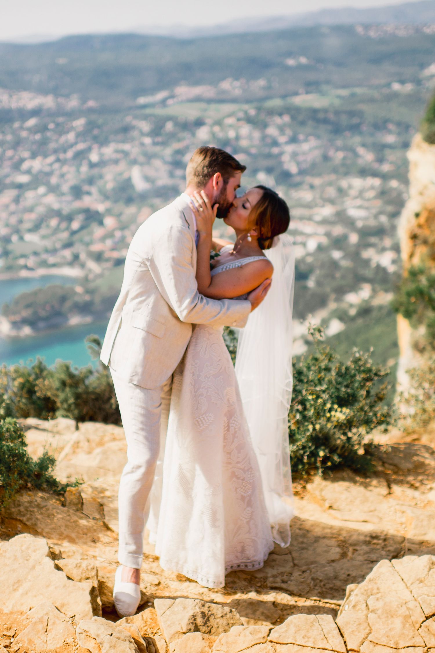 Couple shares romantic moment on clifftop overlooking coastal Mediterranean landscape.