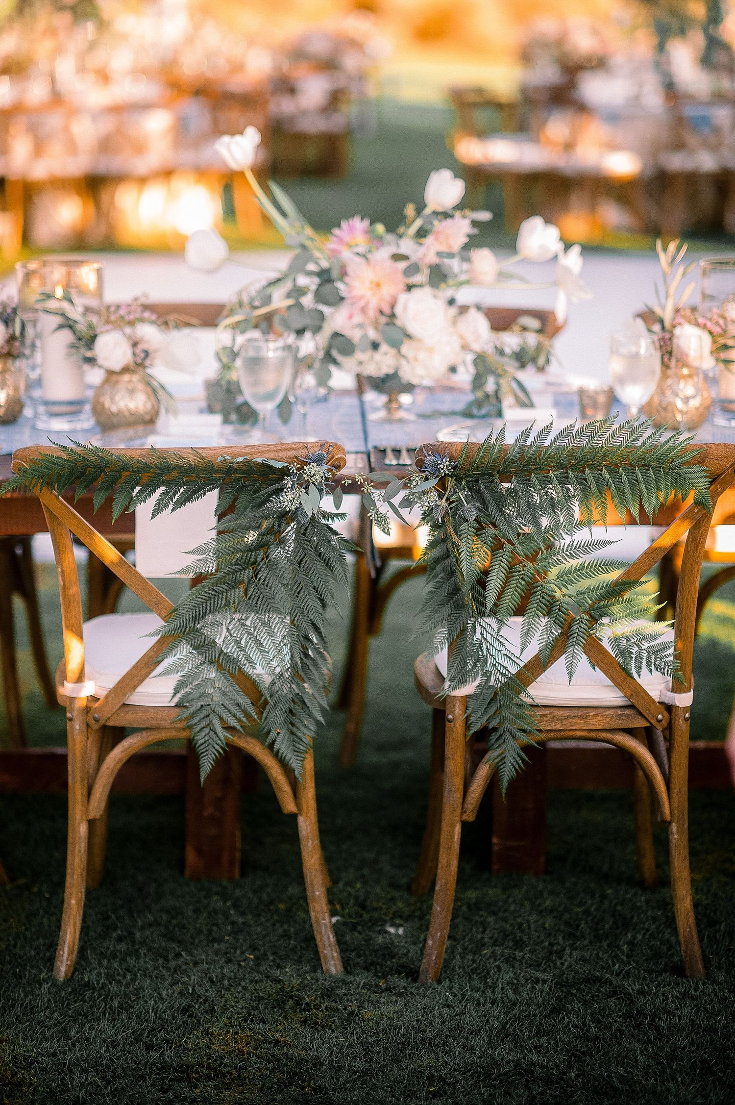 Elegant wedding reception tables decorated with palm fronds and delicate floral arrangements in a romantic setting.