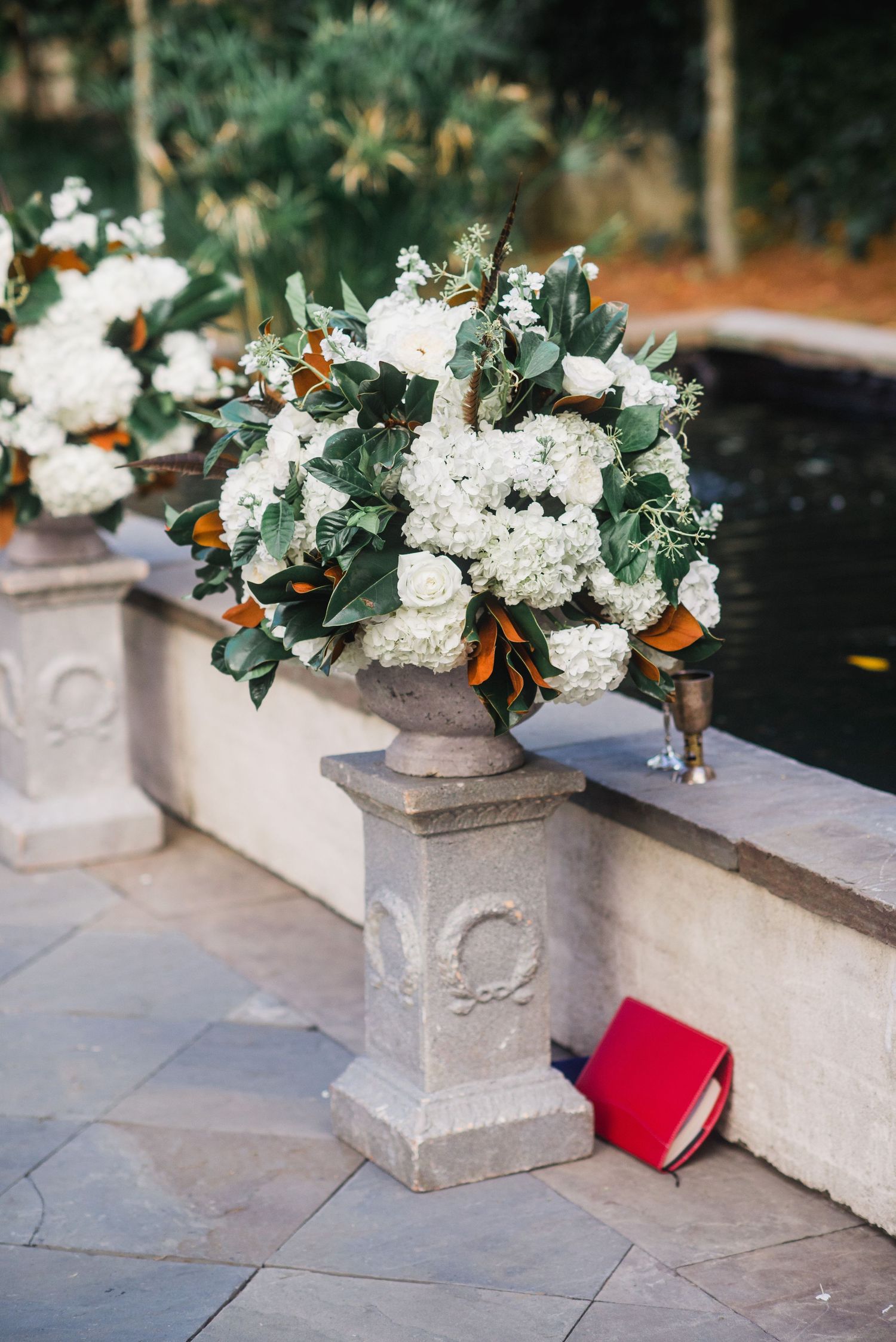 White floral arrangements in concrete planters line a stone ledge with a red accent piece.