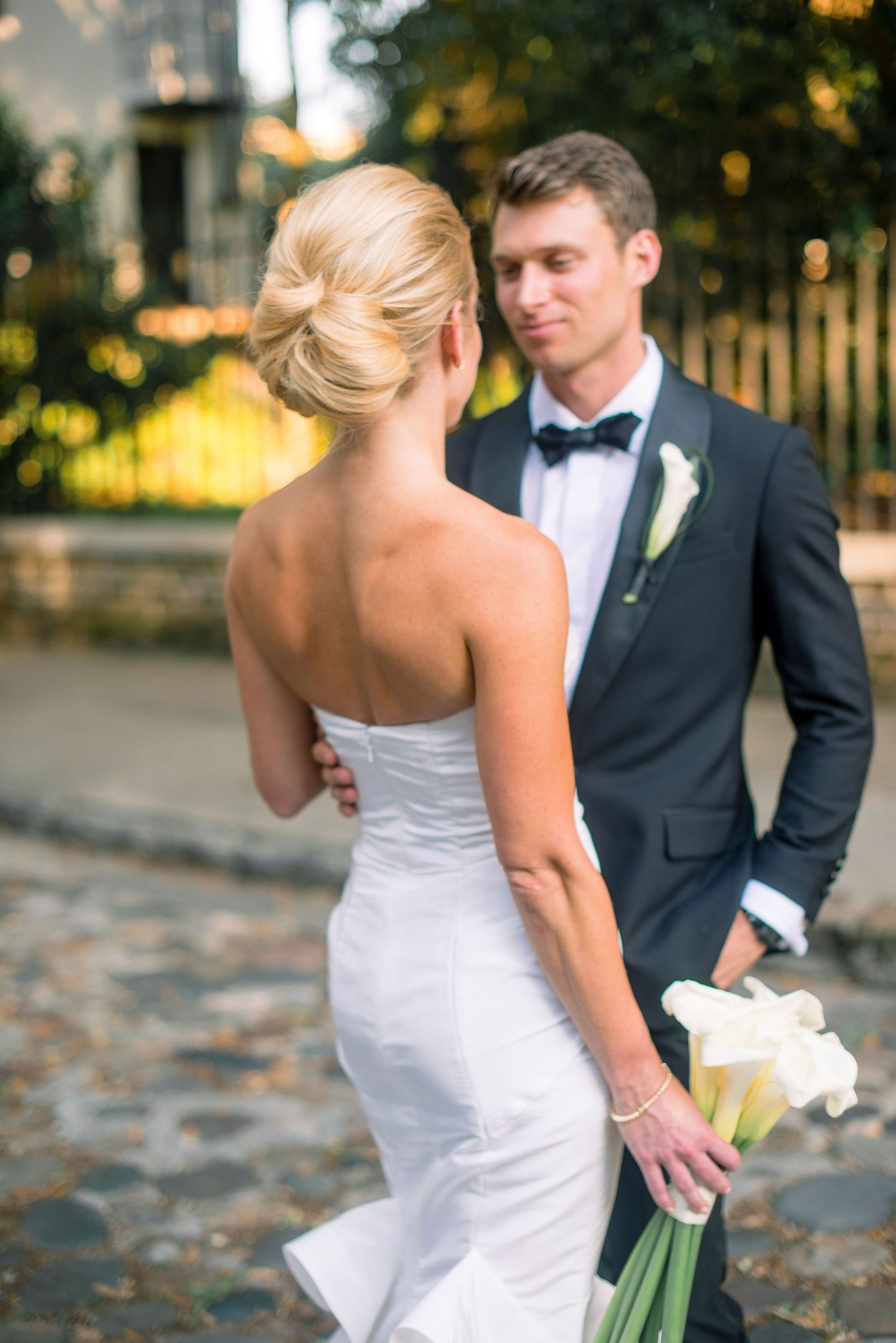 A bride in a white strapless gown and groom in a black tuxedo share a candid moment among autumn leaves.