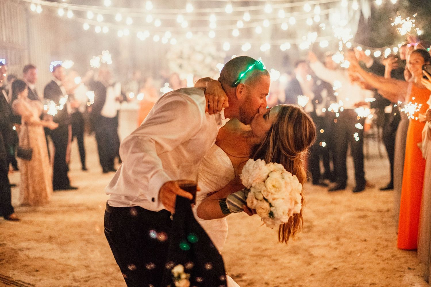 A romantic wedding dance scene with string lights creating a magical glow as guests surround the couple on the dance floor.