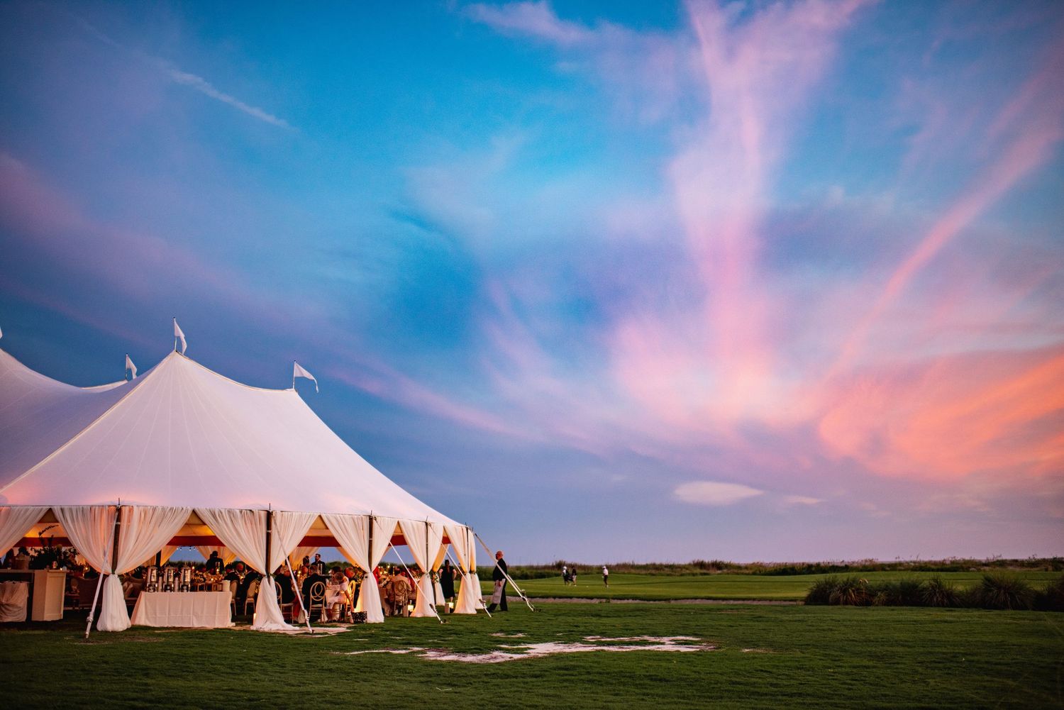 White wedding tents stand against a dramatic pink and blue sunset sky on an open field during golden hour.