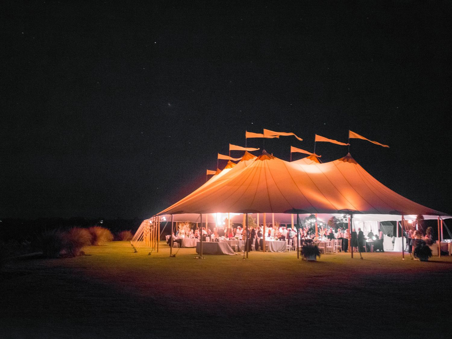 Illuminated festival tents glowing orange and red against the dark night sky during an outdoor event.