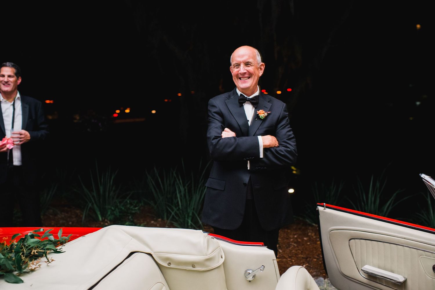 A group of people stand around a white limousine at a formal event in the dark.