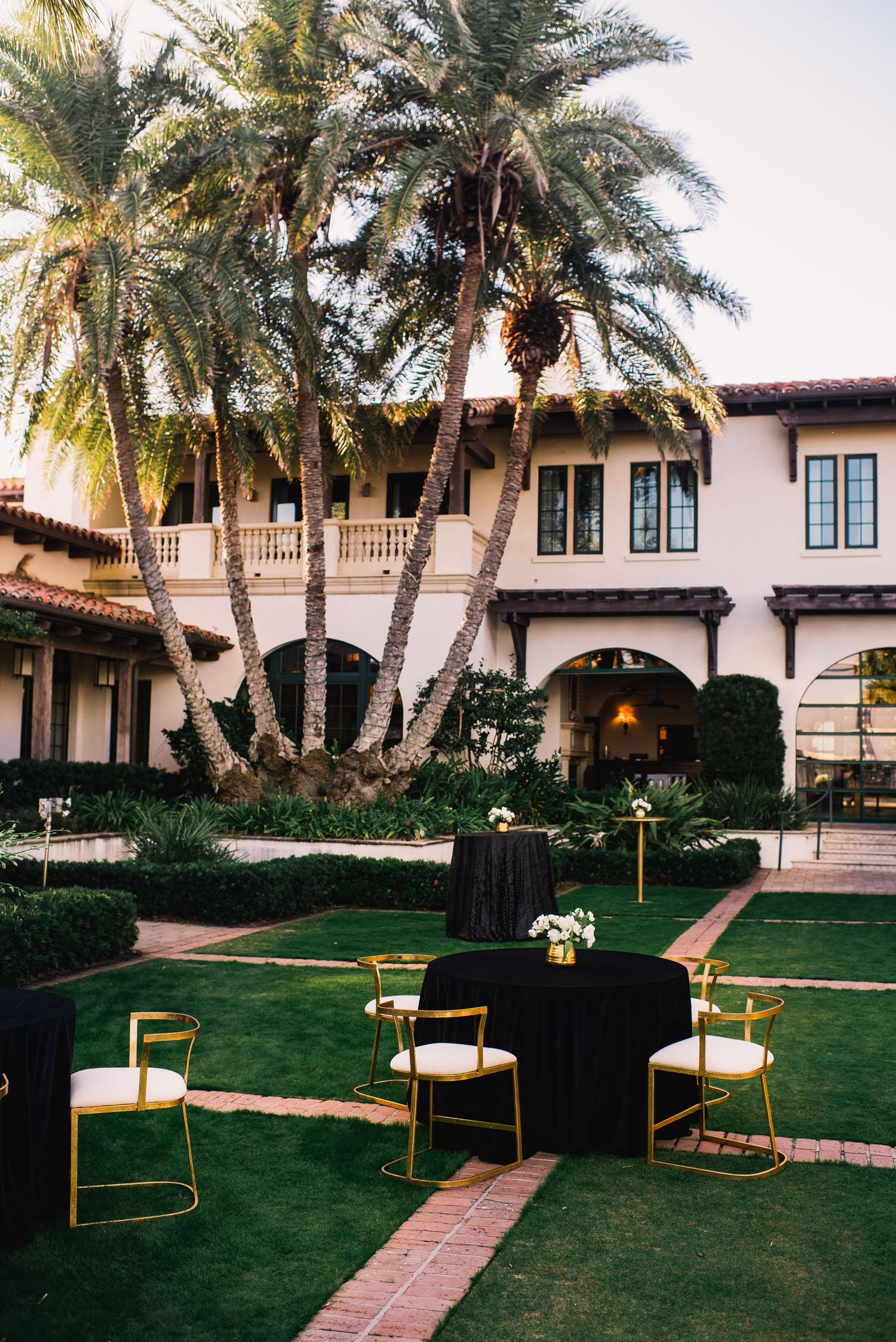 Mediterranean-style villa with palm trees and modern outdoor furniture setup on a manicured lawn.