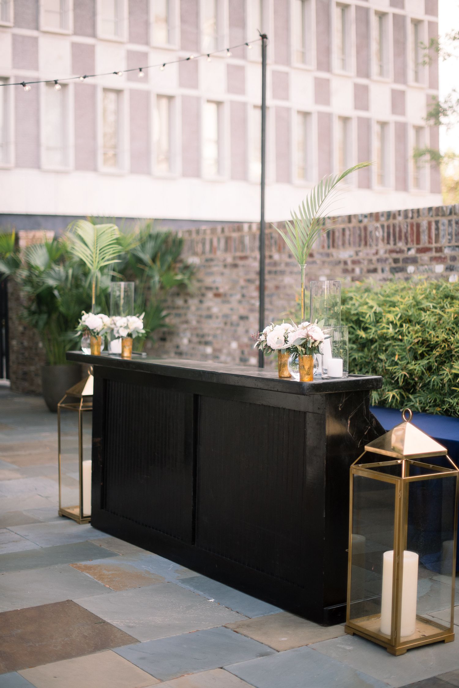 Modern outdoor patio space with black planters and gold accent tables arranged along a stone wall.