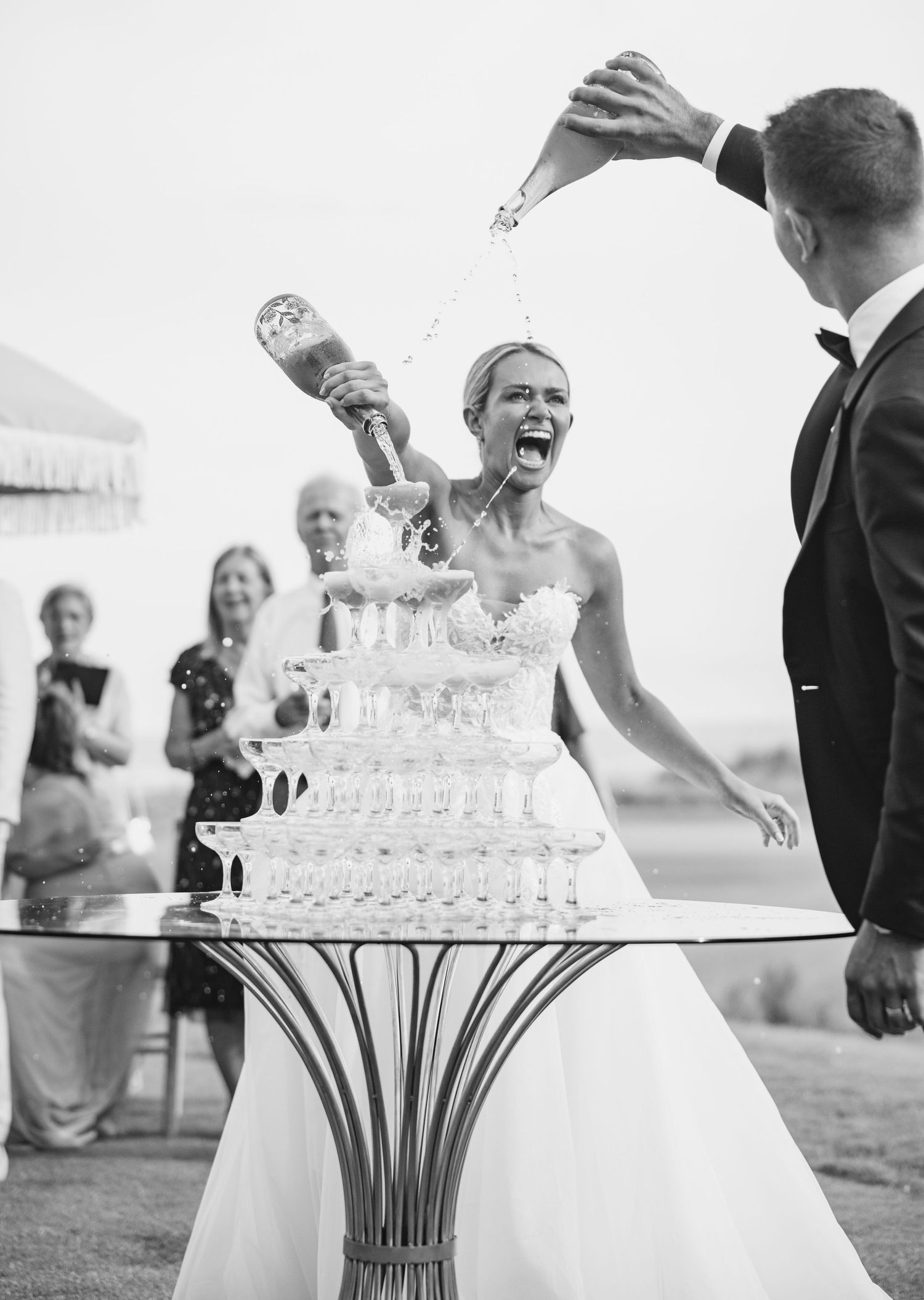 Black and white photo of an elegant tiered wedding cake with champagne tower setup.