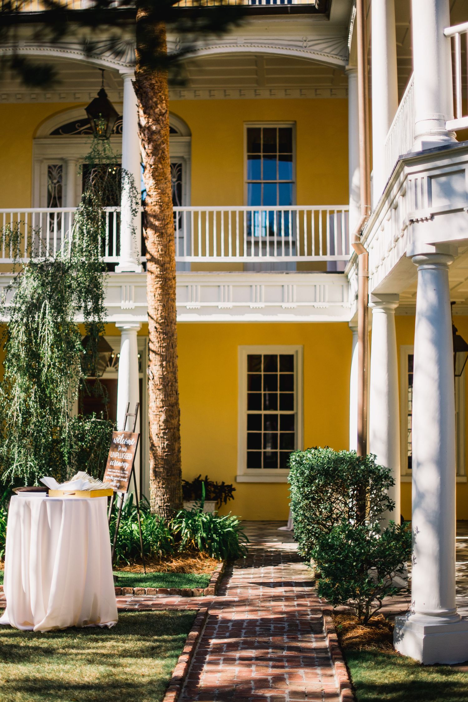 Elegant courtyard with white columns and yellow walls features brick pathways and lush greenery at a historic building.