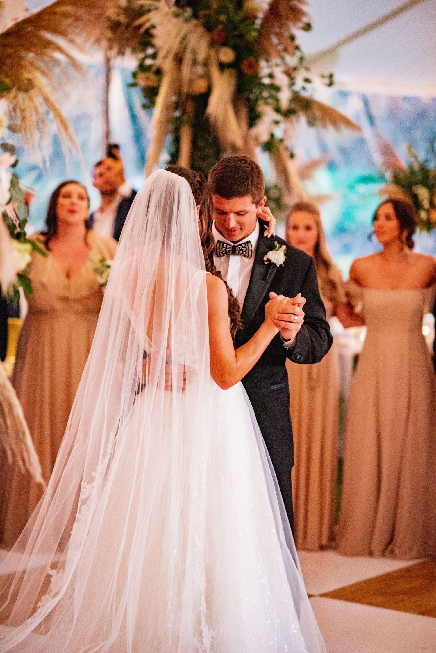 A romantic wedding ceremony scene with flowing white veil and neutral champagne bridesmaids dresses in the background.