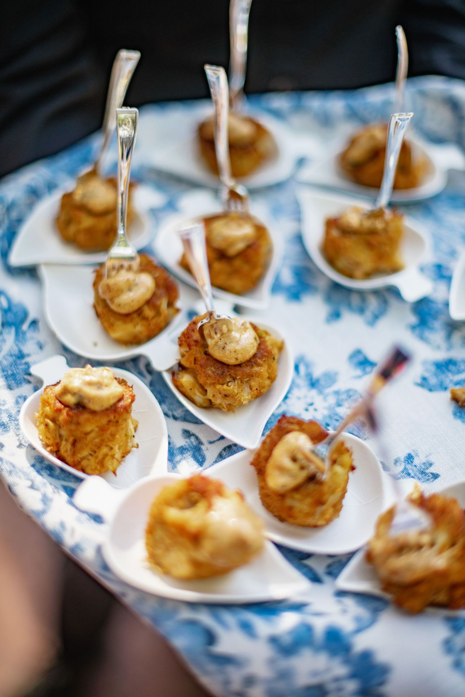 Small appetizer bites with banana and caramel sauce served on white ceramic spoons on a blue and white patterned tablecloth.
