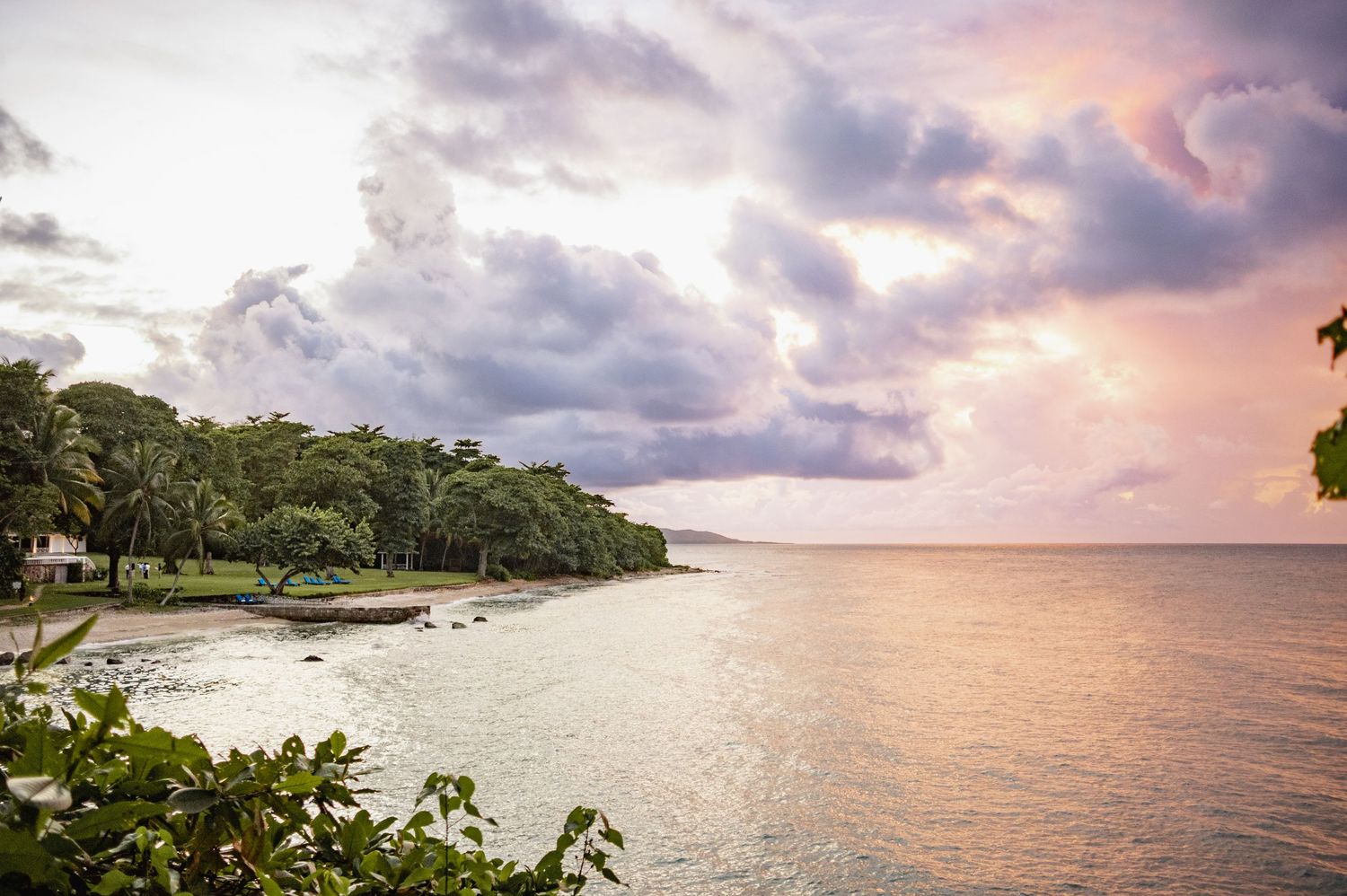 Panoramic view of a tropical beach at sunset with dramatic clouds and palm trees along the shoreline.
