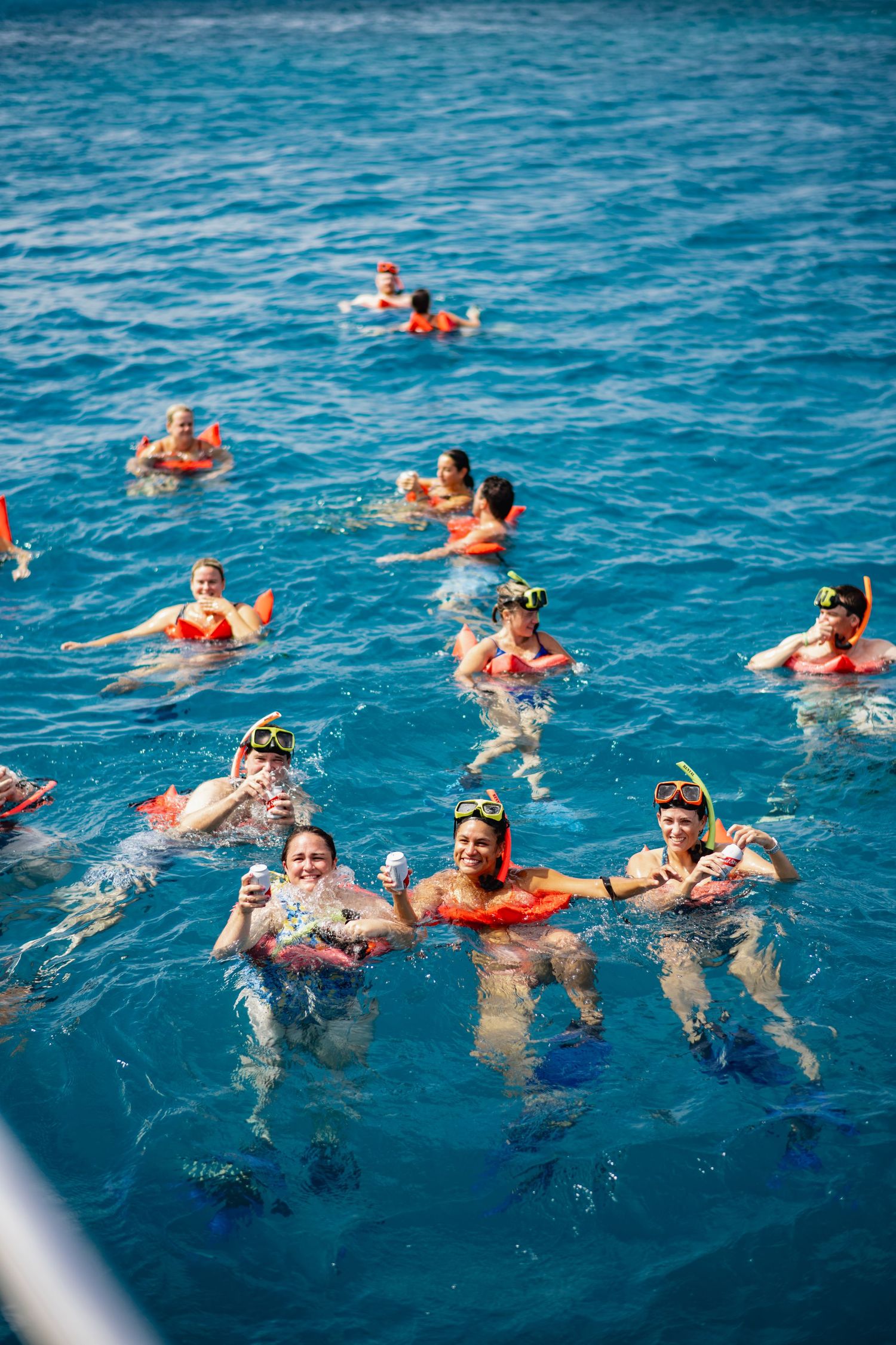 Snorkelers float together in crystal clear turquoise waters wearing orange life vests and masks during ocean excursion.