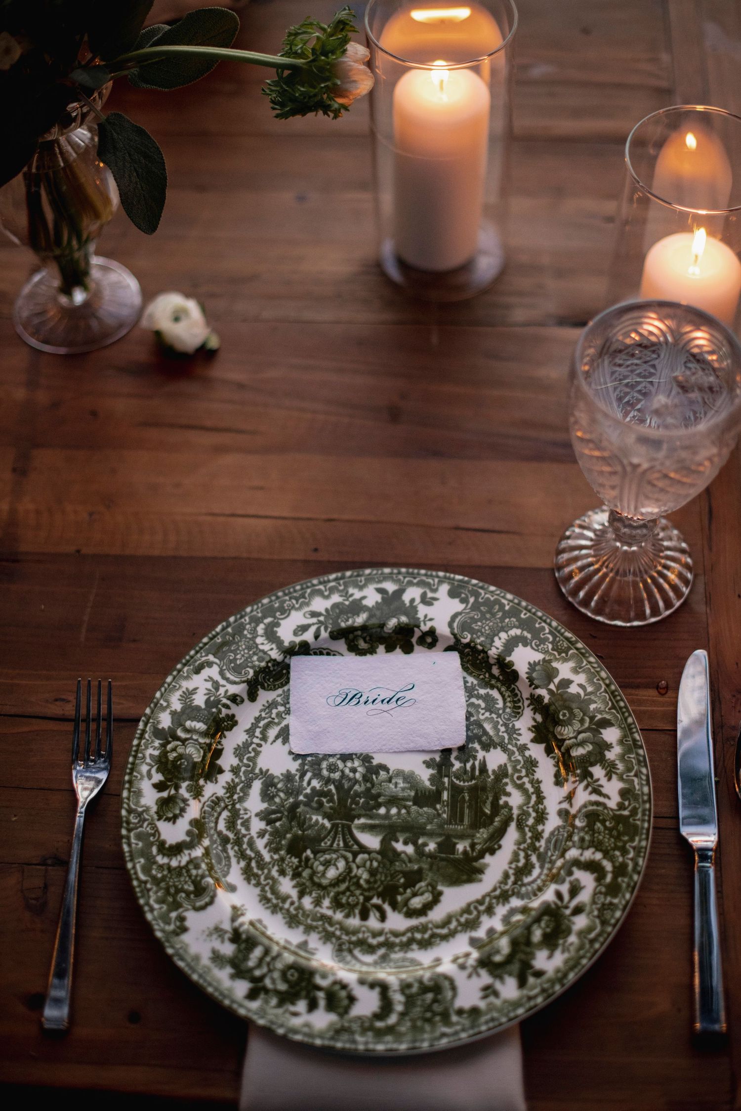 Vintage green and white patterned china plates set on wooden table with glowing candles for formal dining.