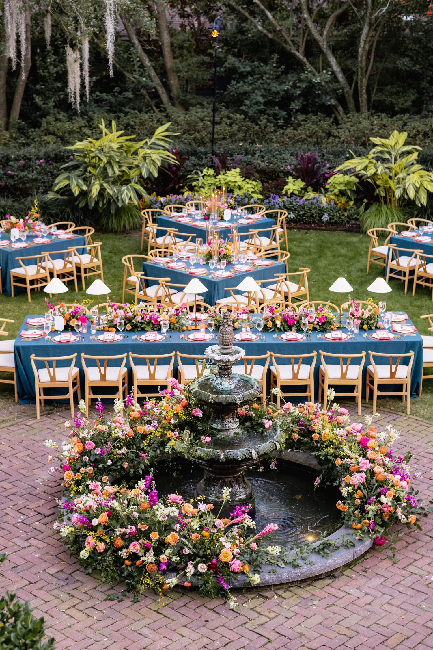 Elegant outdoor wedding reception setup with round tables adorned with vibrant pink and coral floral arrangements on brick patio.