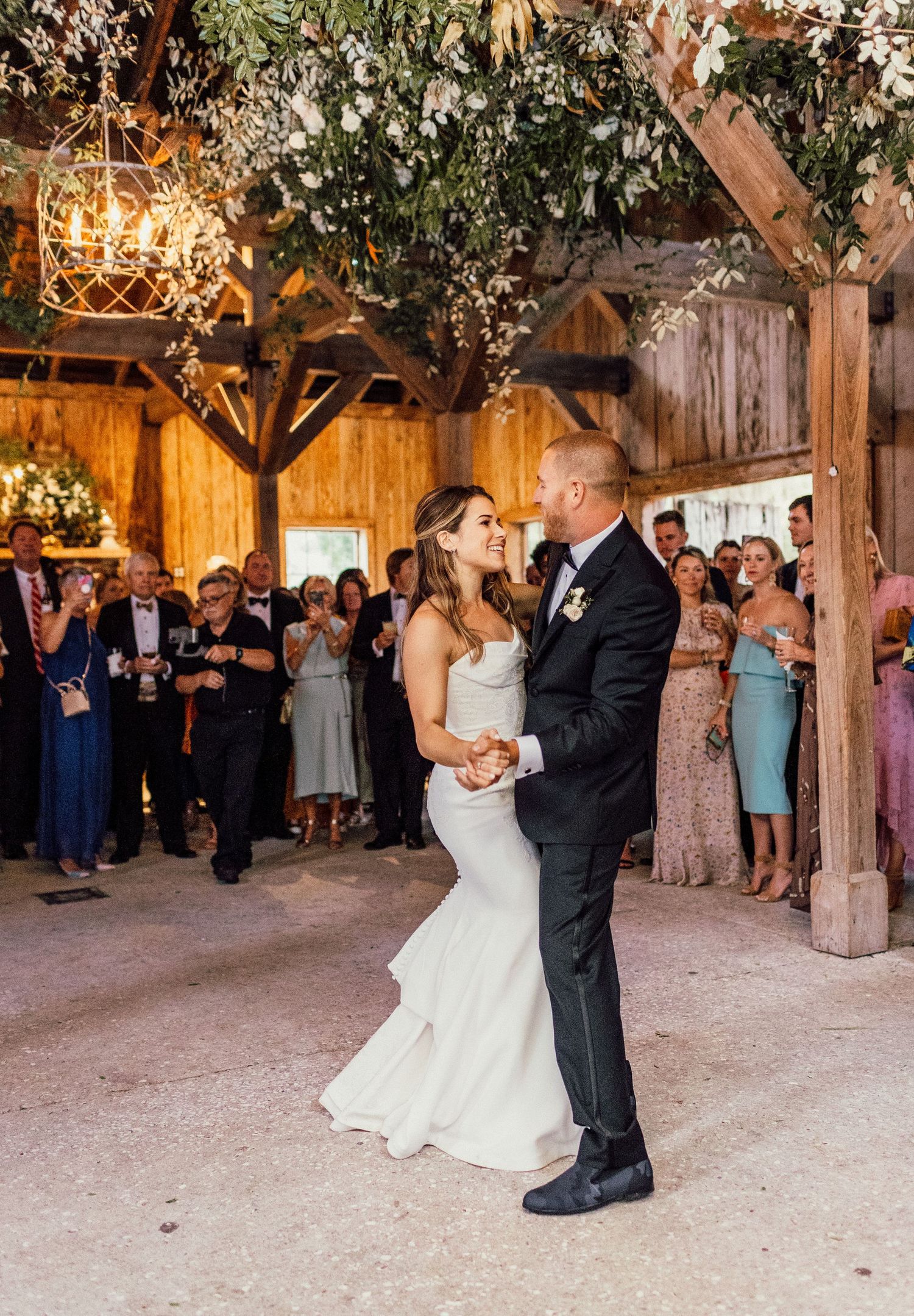 Romantic first dance sequence of newlyweds in a rustic barn venue with guests watching from the sidelines.