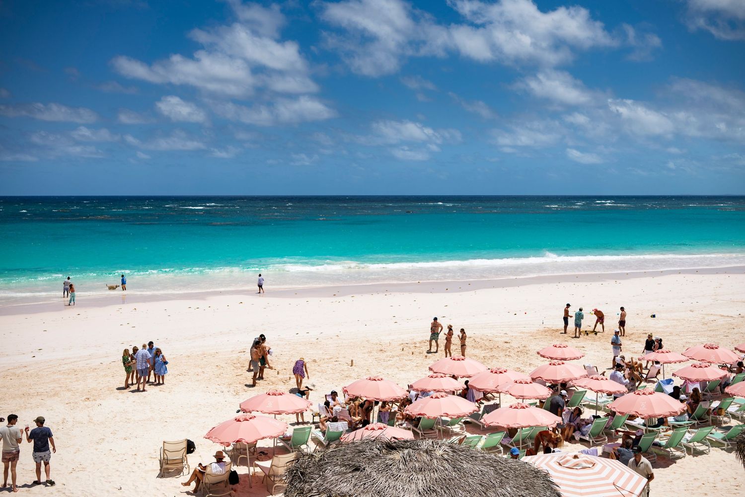 Tourists enjoying a pristine white sand beach with crystal clear turquoise waters and blue skies in the Caribbean.