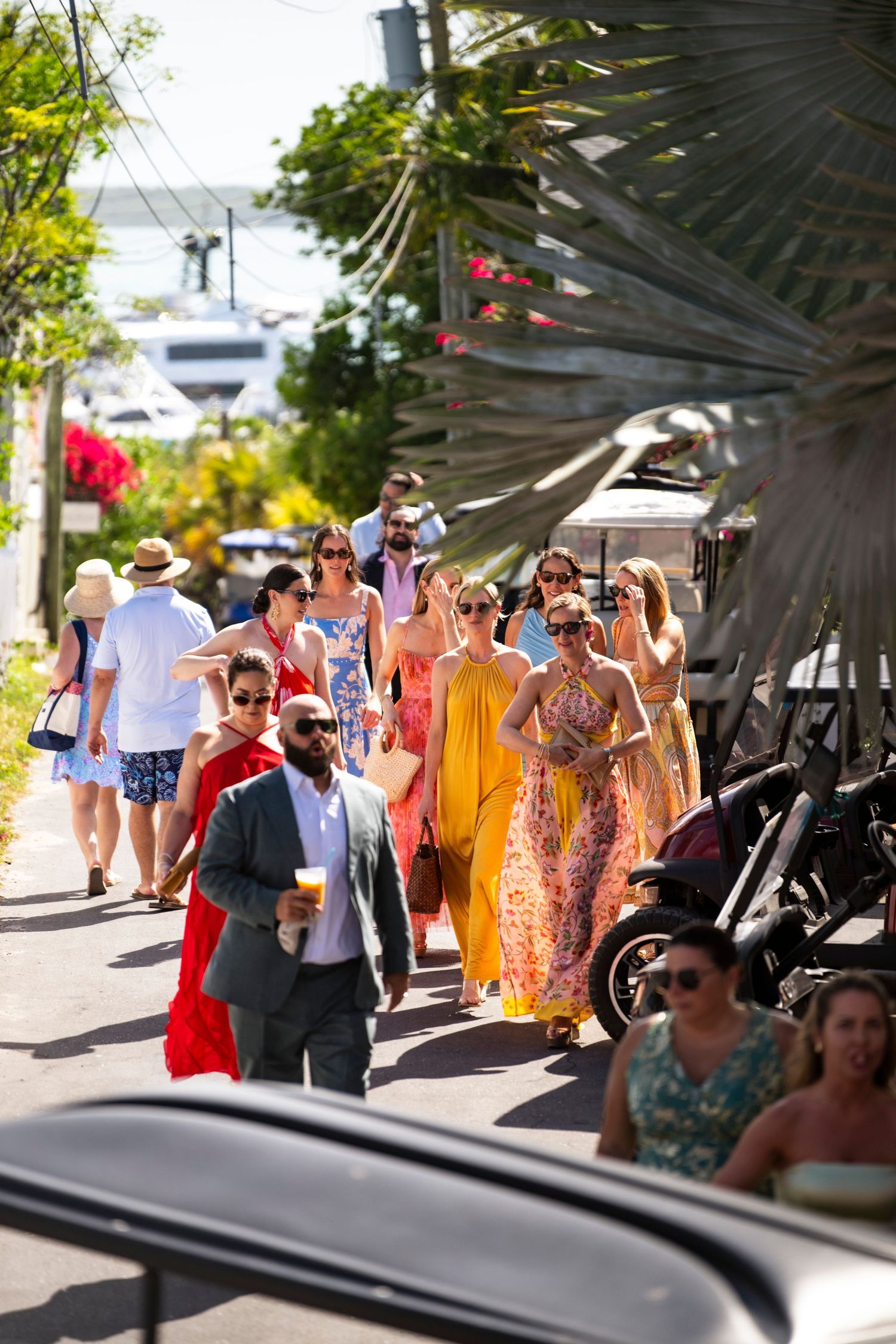 A group of tourists in colorful summer dresses and casual attire walking along a sunny outdoor path.