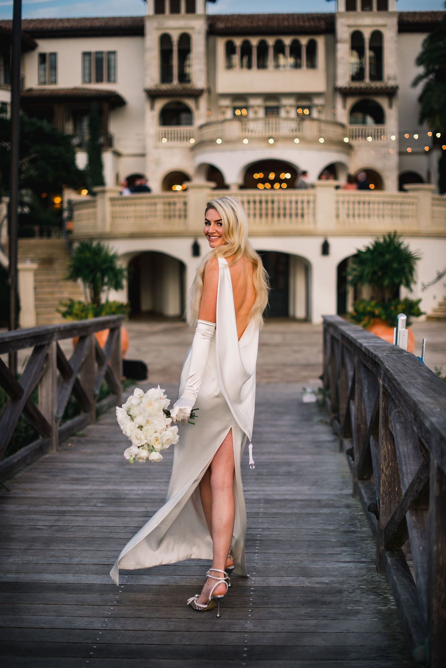 Elegant bridal portraits on a wooden boardwalk with Mediterranean-style architecture in the background.
