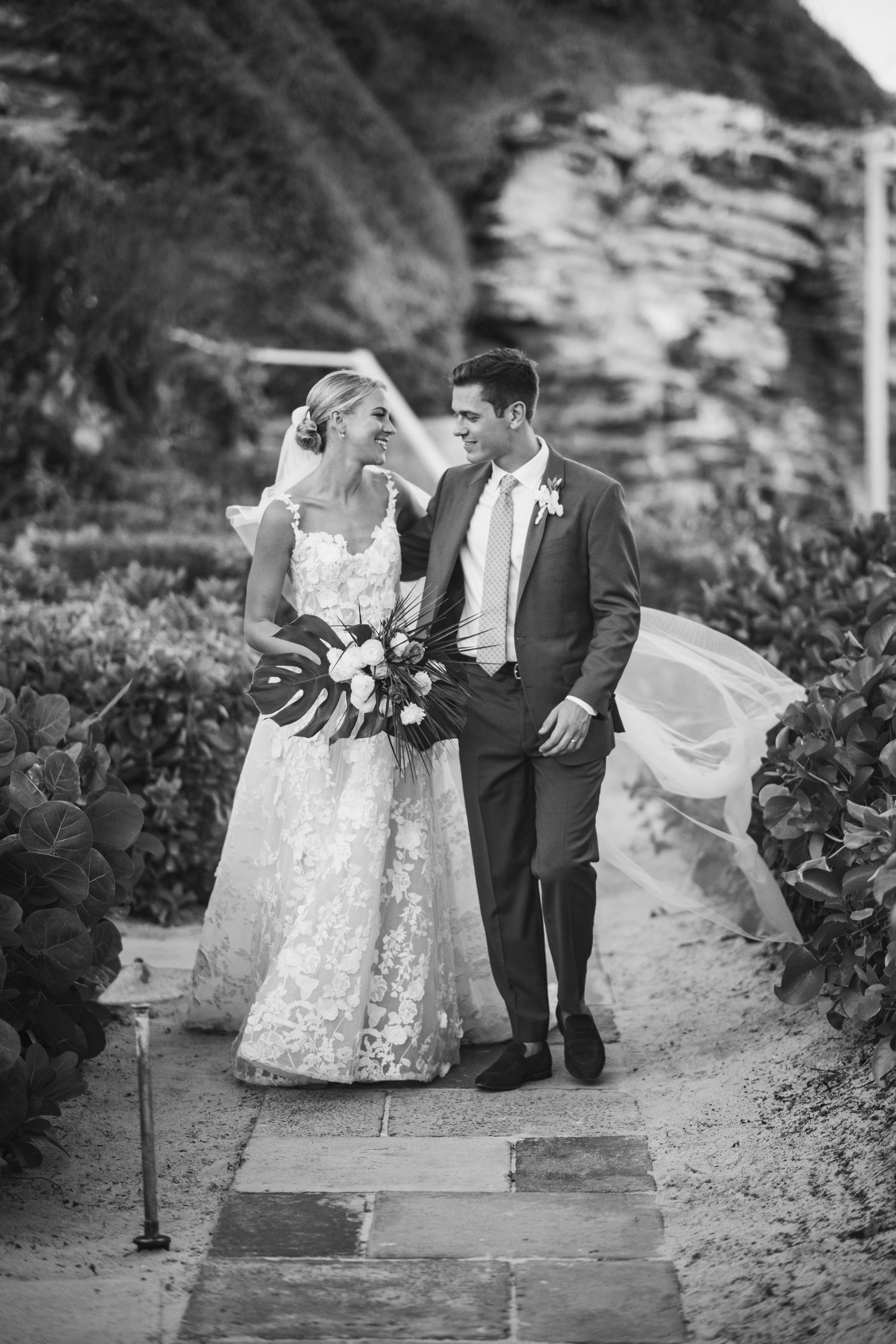 Black and white photo of a couple walking along a stone path surrounded by foliage.